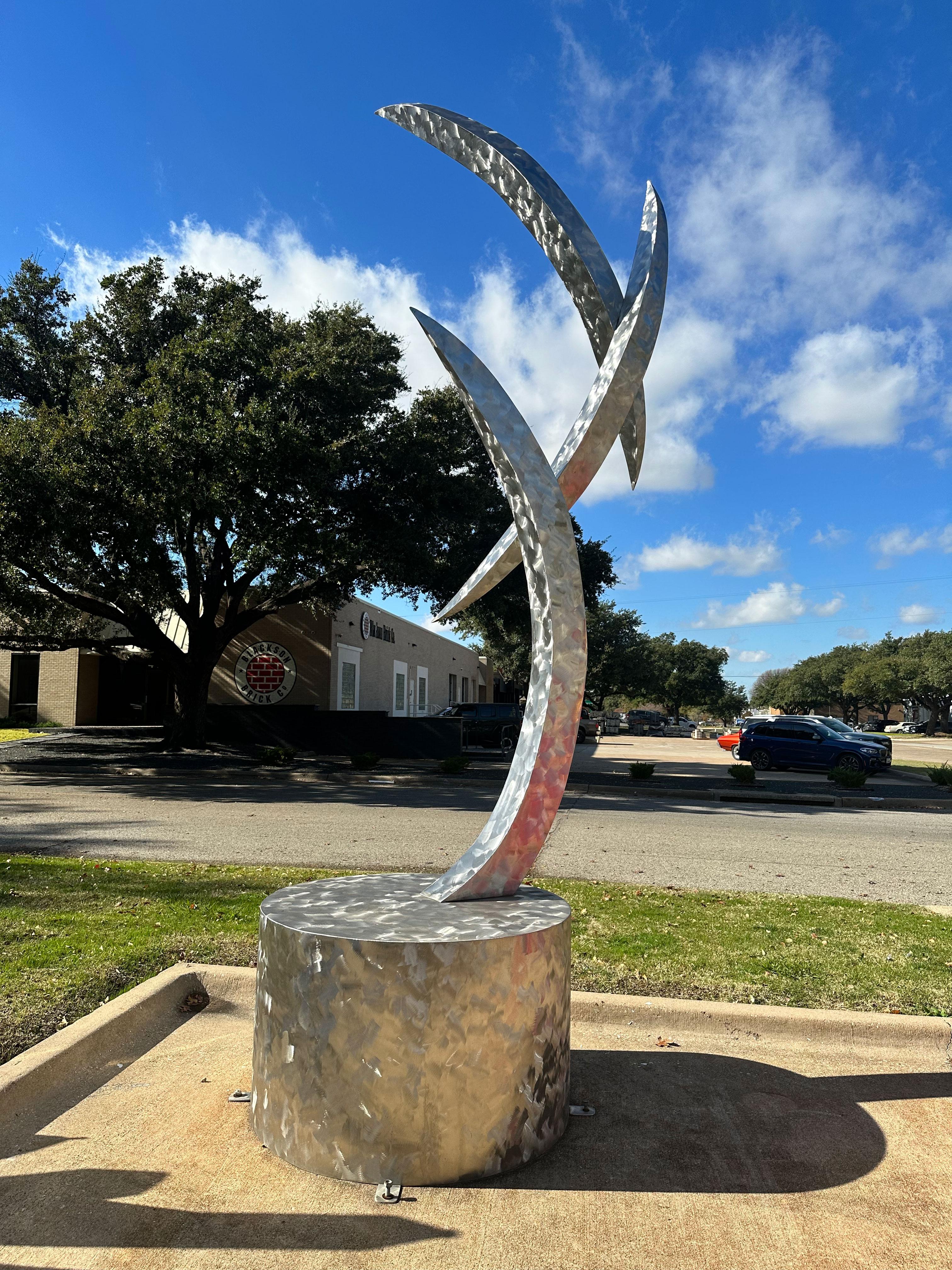 "We Three" by Jerry Dane Sanders is a large brushed finish stainless steel outdoor sculpture measuring 180x72x72. Crafted from high-quality stainless steel, this piece features three pillars that sway gracefully between each other, creating a