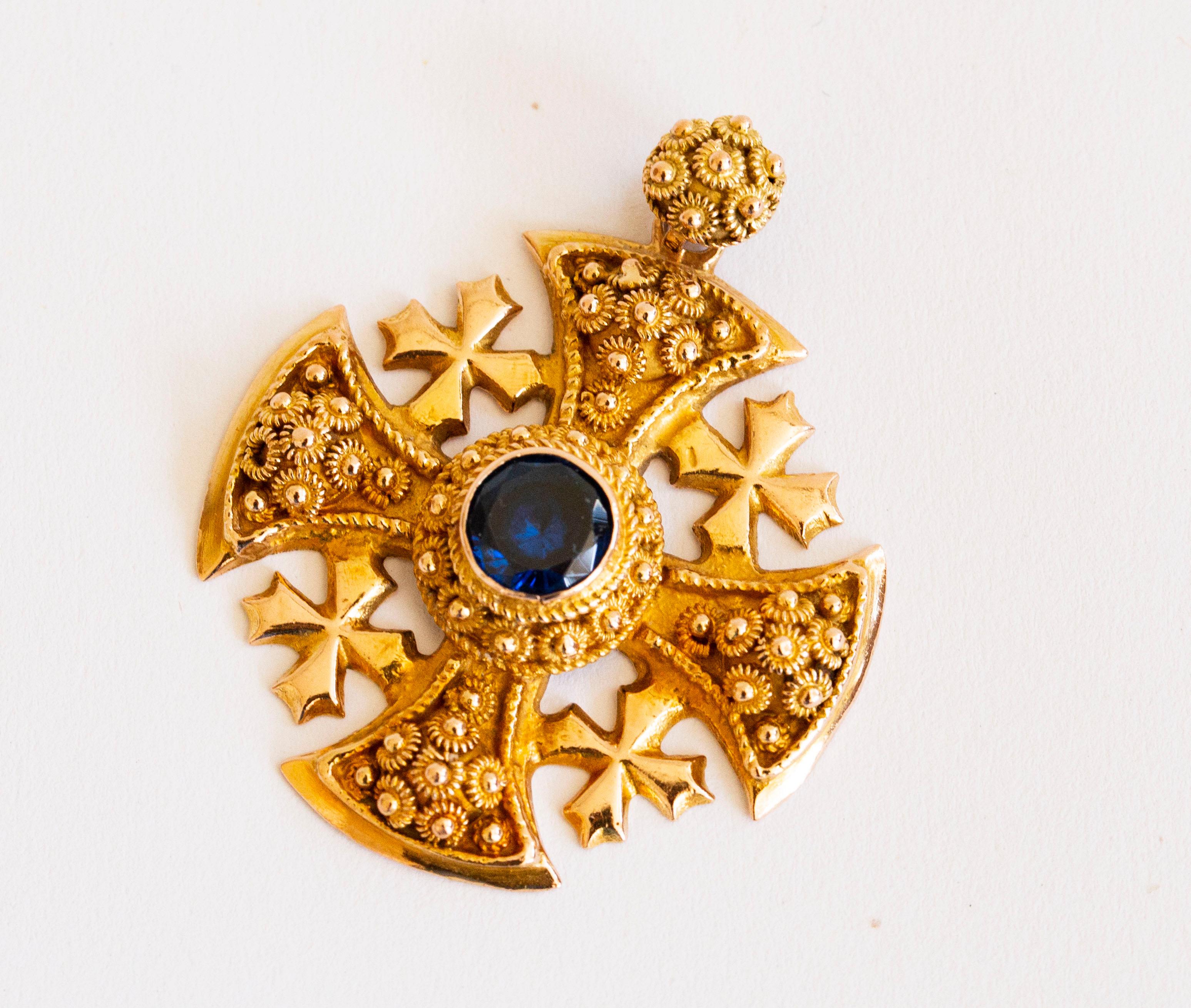 A vintage Jerusalem Crusaders Cross Pendant made of 14 karat yellow gold with a blue stone. The pendant features the Etruscan Revival style with the characteristic rich decoration of cannetille, rosettes and wirework. The pendant is marked with 14K