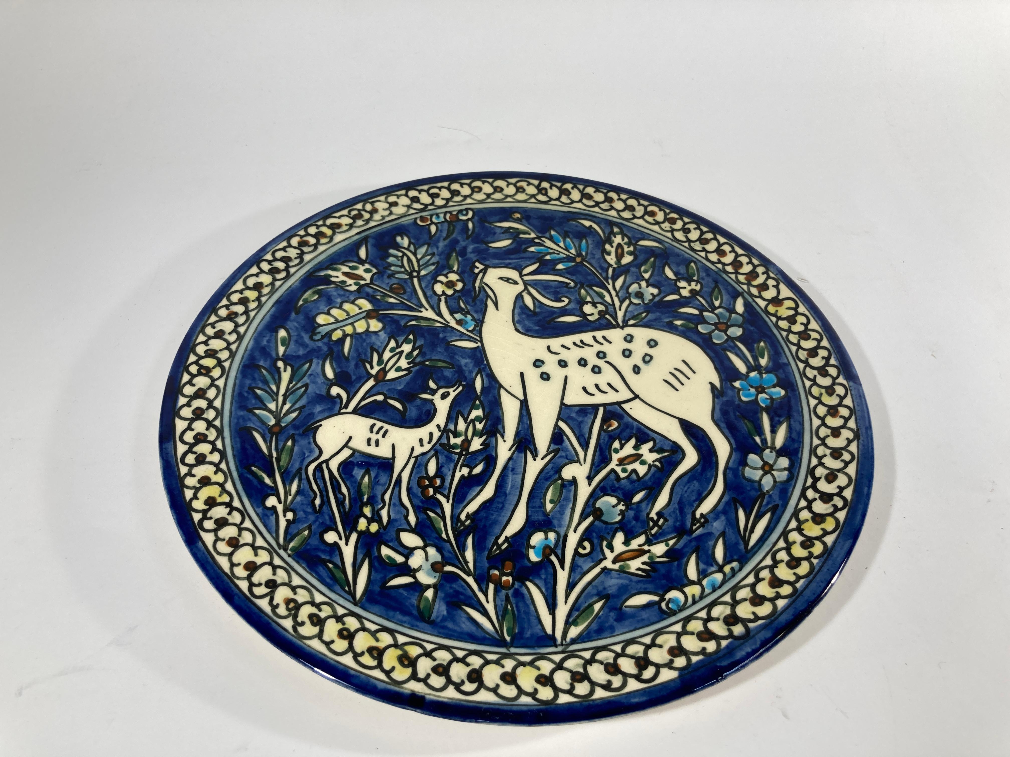 Vintage hand painted and handcrafted ceramic wall decorative plate with polychrome deer scene. 
It has a beautifully hand painted scene with deers enjoying the outdoors , surrounded by flowers in blue and white, turquoise, light and dark green