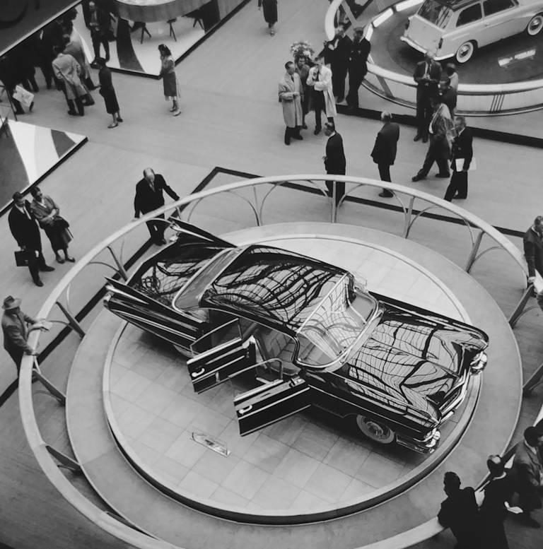 Salon de l'automobile de Paris - General Motors Design/One par Jess Alexander est un tirage pigmentaire d'archives de 14 x 14 pouces. Cette photographie représente une voiture noire exposée, entourée de personnes. Le format du papier est de 22 x 17