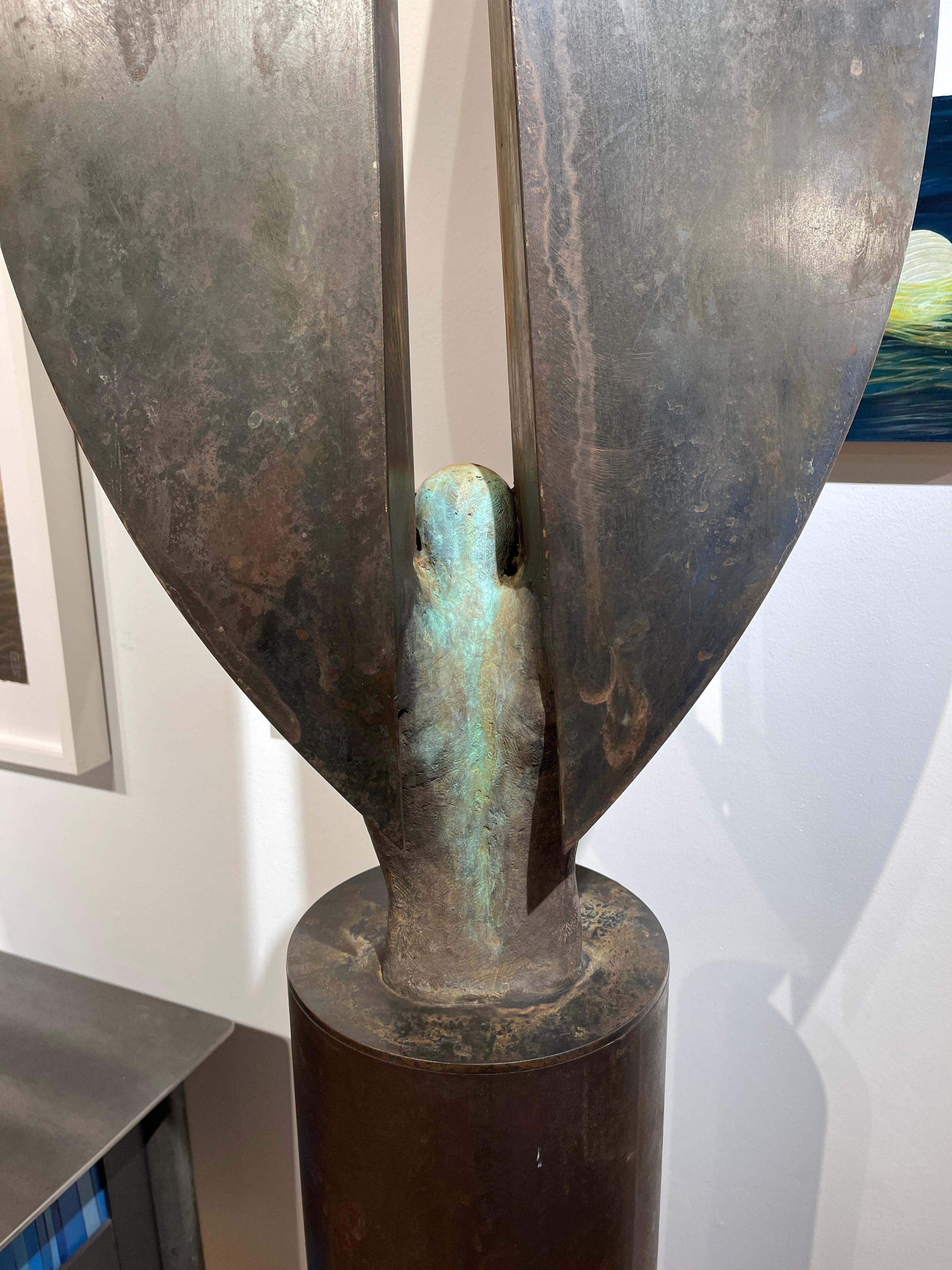 This tall bronze and steel sculpture sits atop a cylindrical column base.  The subtle features in the figure contrast against the abstracted geometric wings which reach high into the air.  The finish is a textured rust brown patina.

Jesús Curiá