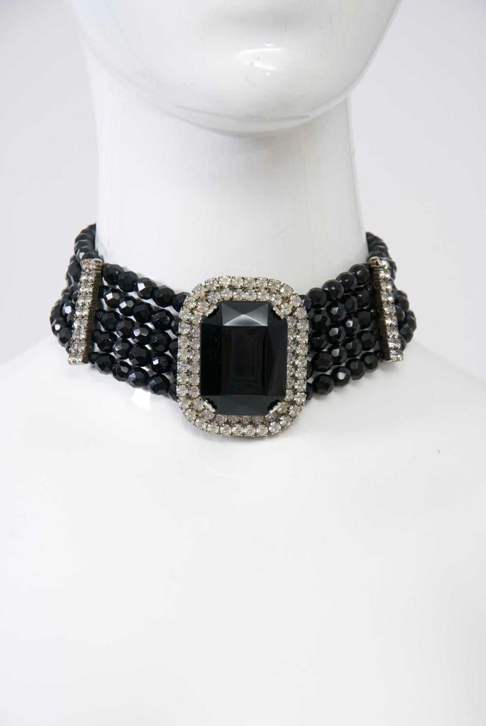 C.1970s wide choker composed of five strands of faceted black glass beads accented by vertical rhinestone bars at each side and centering a large rectangular black stone surrounded by rhinestones. Adjustable chain closure expands from 12”-15.5”;