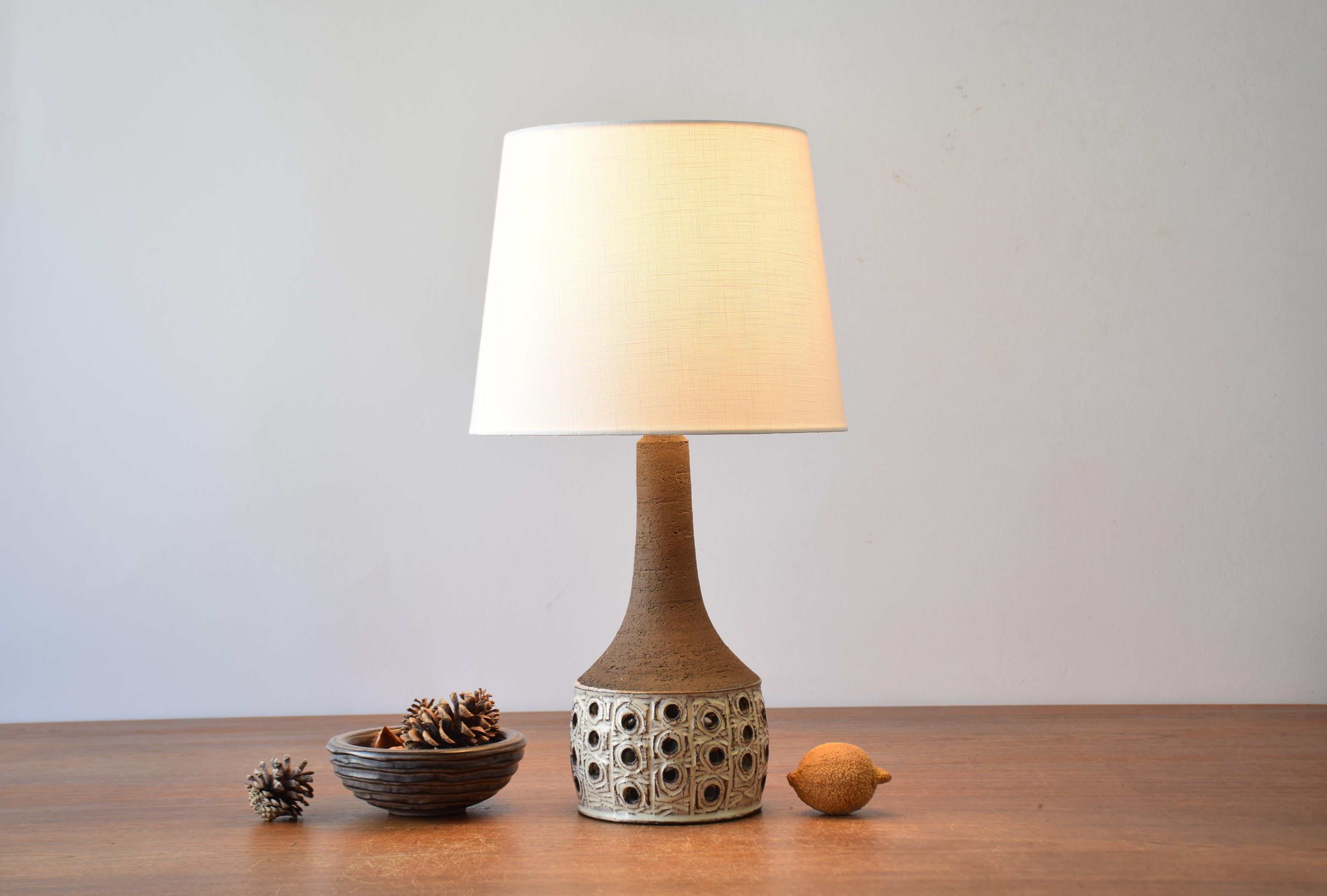 Midcentury ceramic table lamp by Danish ceramist Jette Hellerøe, ca 1970s.
The body of the lamp is decorated with a laced circle decor with beige glaze contrasted by the unglazed dark brown neck. The lamp is made with chamotte clay which gives a