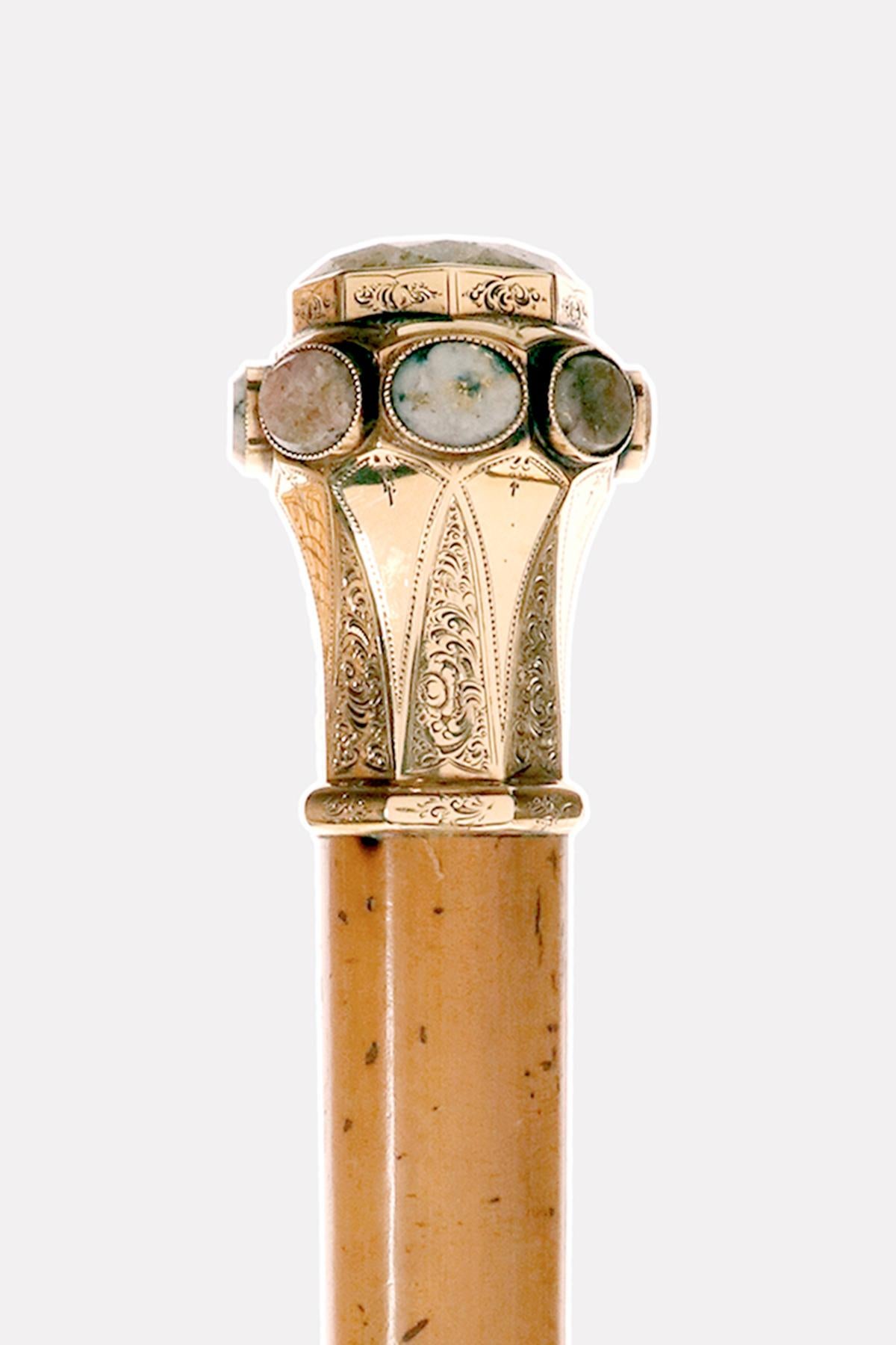 Bastón: bastón enjoyado, pomo octogonal en forma de milord de oro de 16 kt con en la parte superior un gran cuarzo central octogonal dorado y 8 laterales ovalados de distintos colores. Caña de madera de Malaca. Punta de metal Se trata de un bastón
