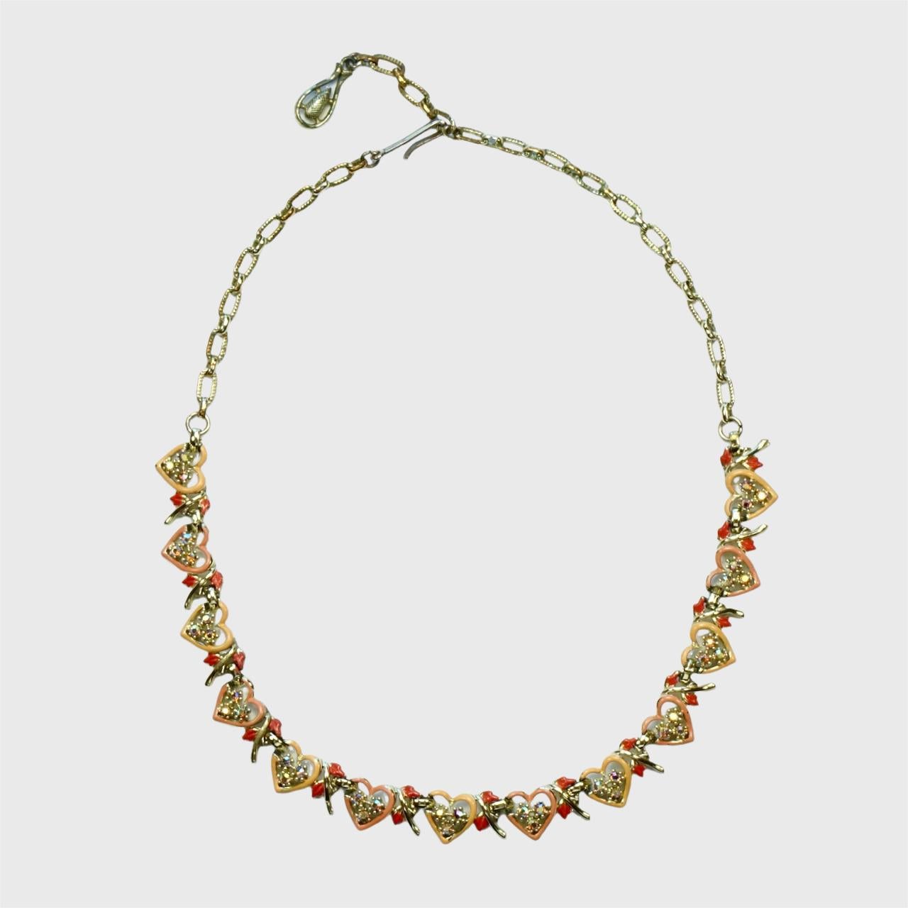 Jewelcraft pale gold plated peach and red enamel heart necklace, bracelet and earrings set. Each enamel heart is set with three aurora borealis rhinestones. There is wear to the gold plating and enamel.

The necklace measures length 40.5 cm / 15.9