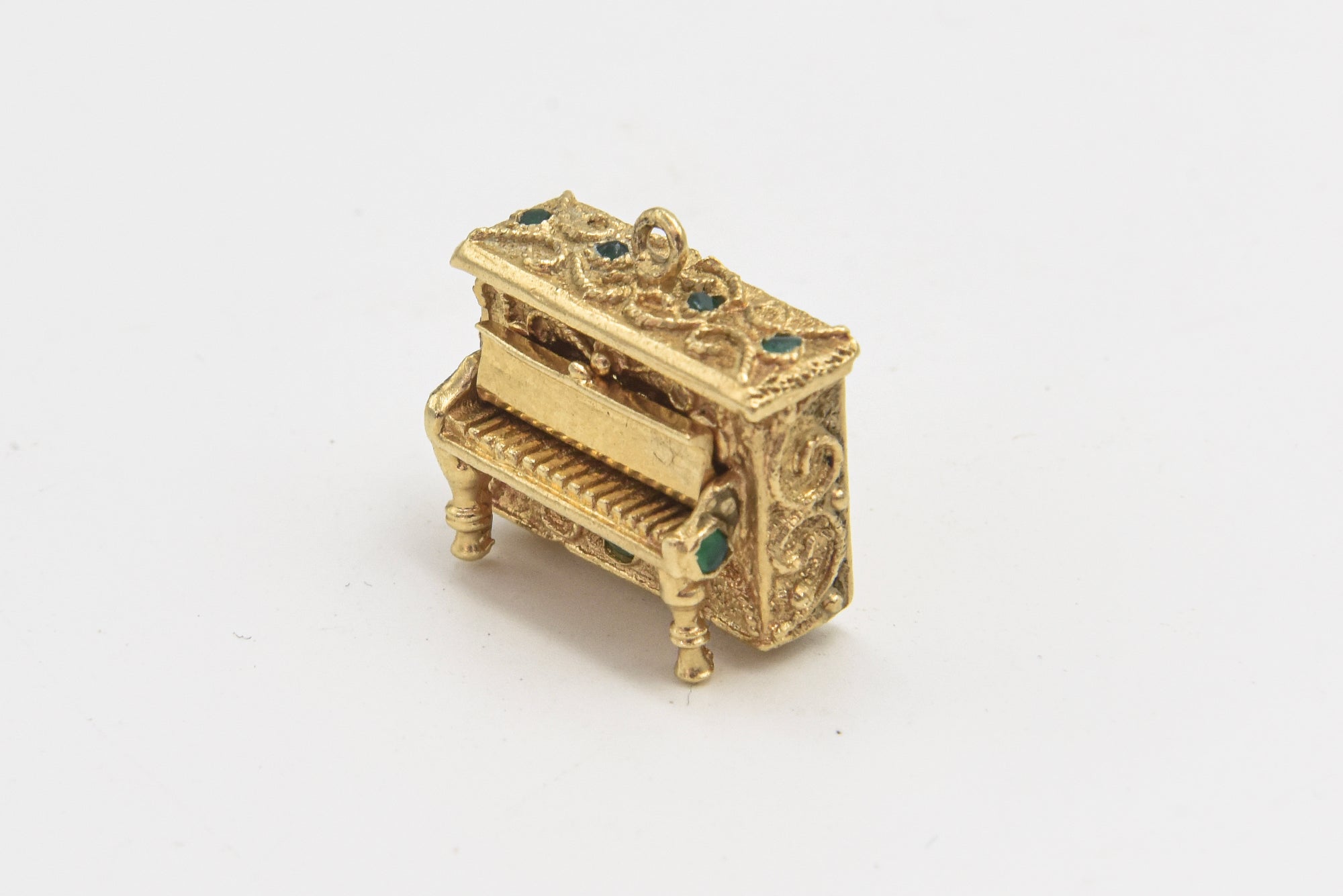 14k Yellow gold figural gold piano charm that features a hinged cover that reveals articulated piano keys, bezel-set chrysoprase cabochons, and applied rope and granulation details throughout.  It has a bail to the top that allows it to be worn as a