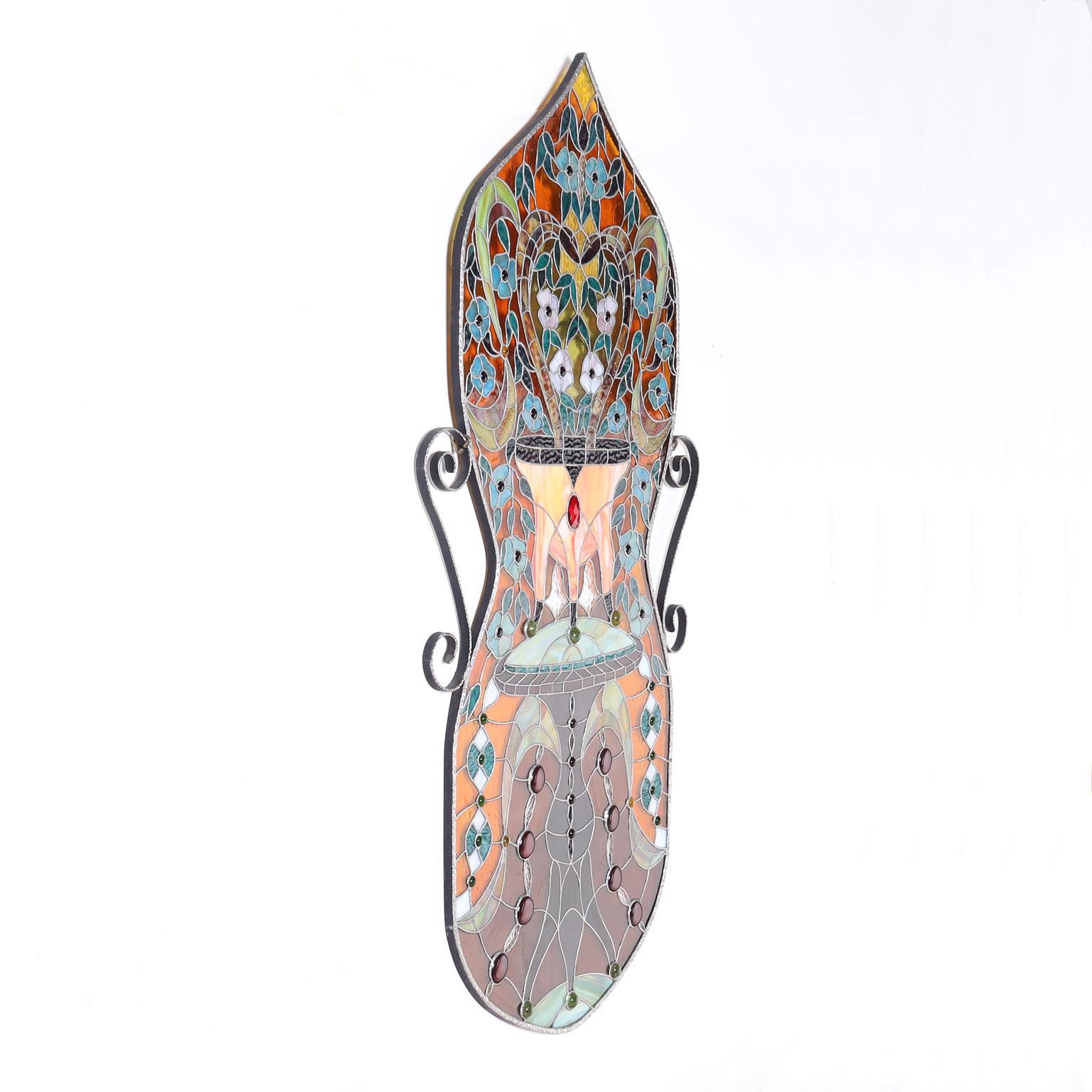 Striking stained glass panel hand crafted in an hourglass form in alluring vivid colors and highlighted with jewels in a festive floral motif.