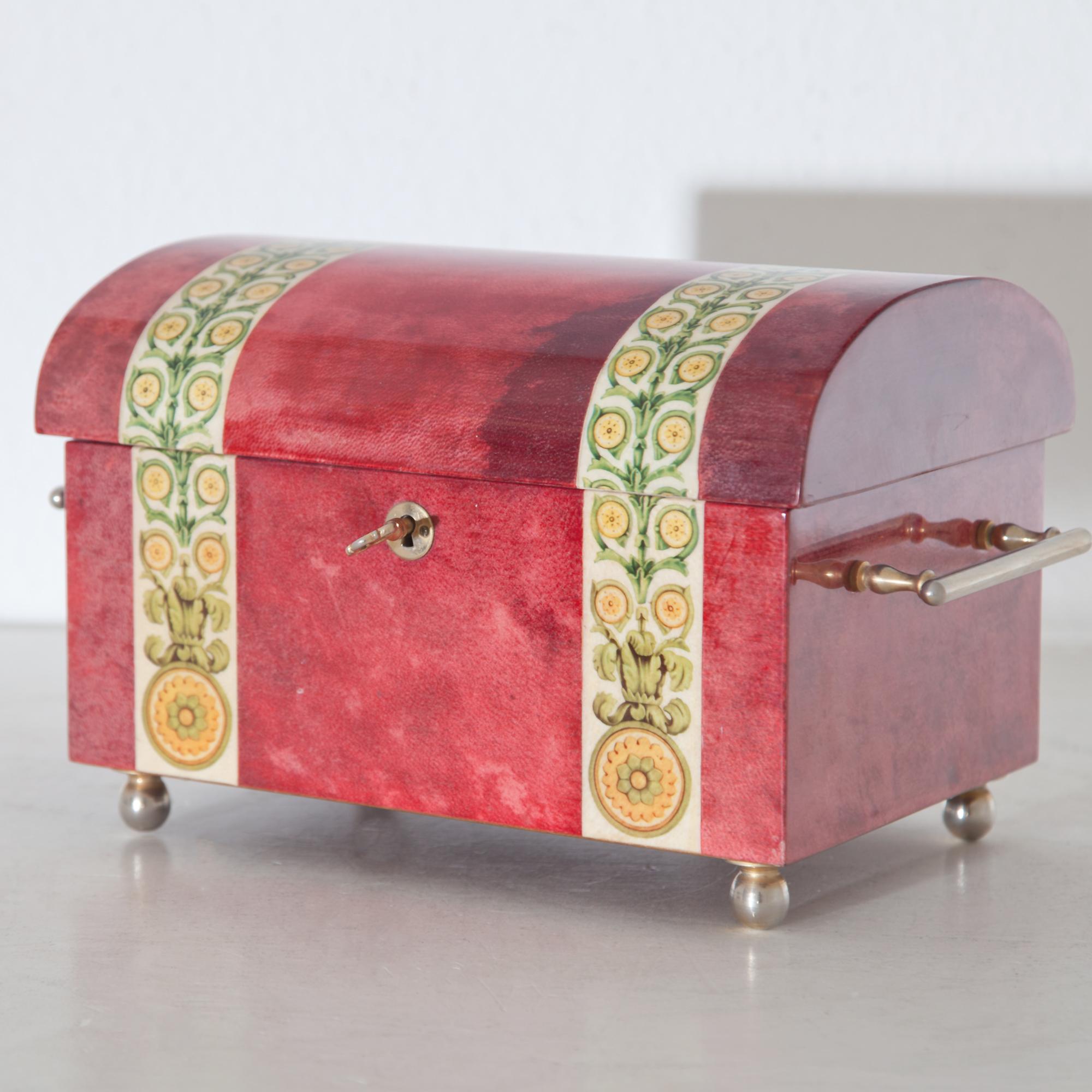 Small box with rounded lid and brass handles. The interior is laid out in velvet and fitted with shelves. Outside covered with red coloured goatskin and clear varnish and printed with floral decor.