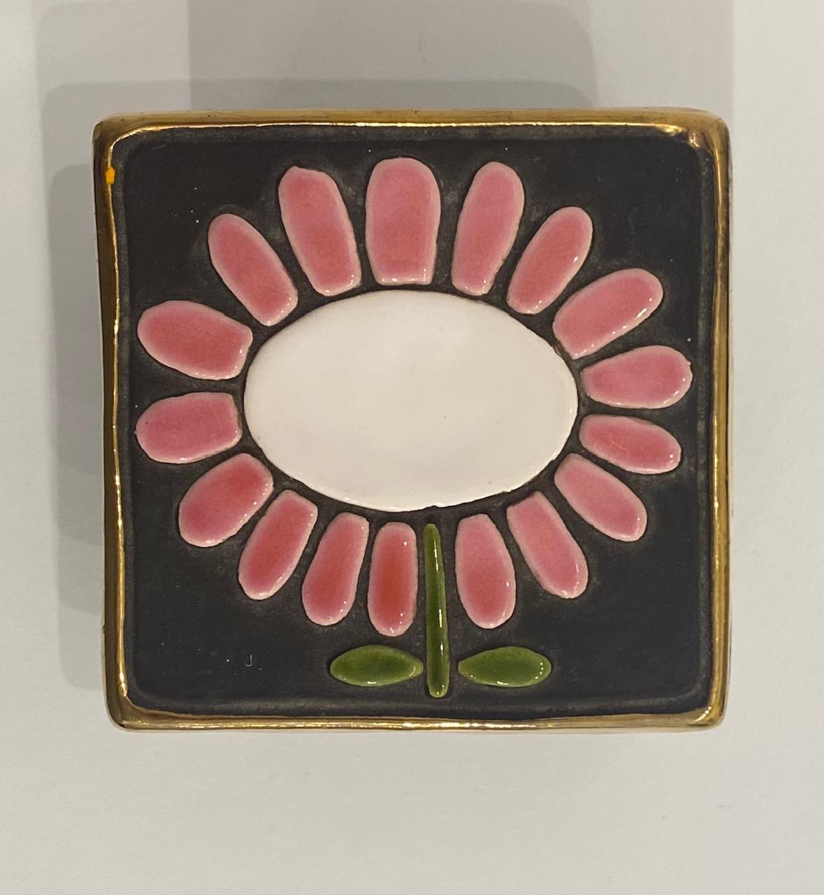 La céramiste française nous invite à contempler la beauté des objets du quotidien à travers un motif émaillé de marguerites roses et blanches, ornant une boîte à bijoux carrée. L'objet traduit la délicatesse inhérente à la féminité, ainsi qu'une