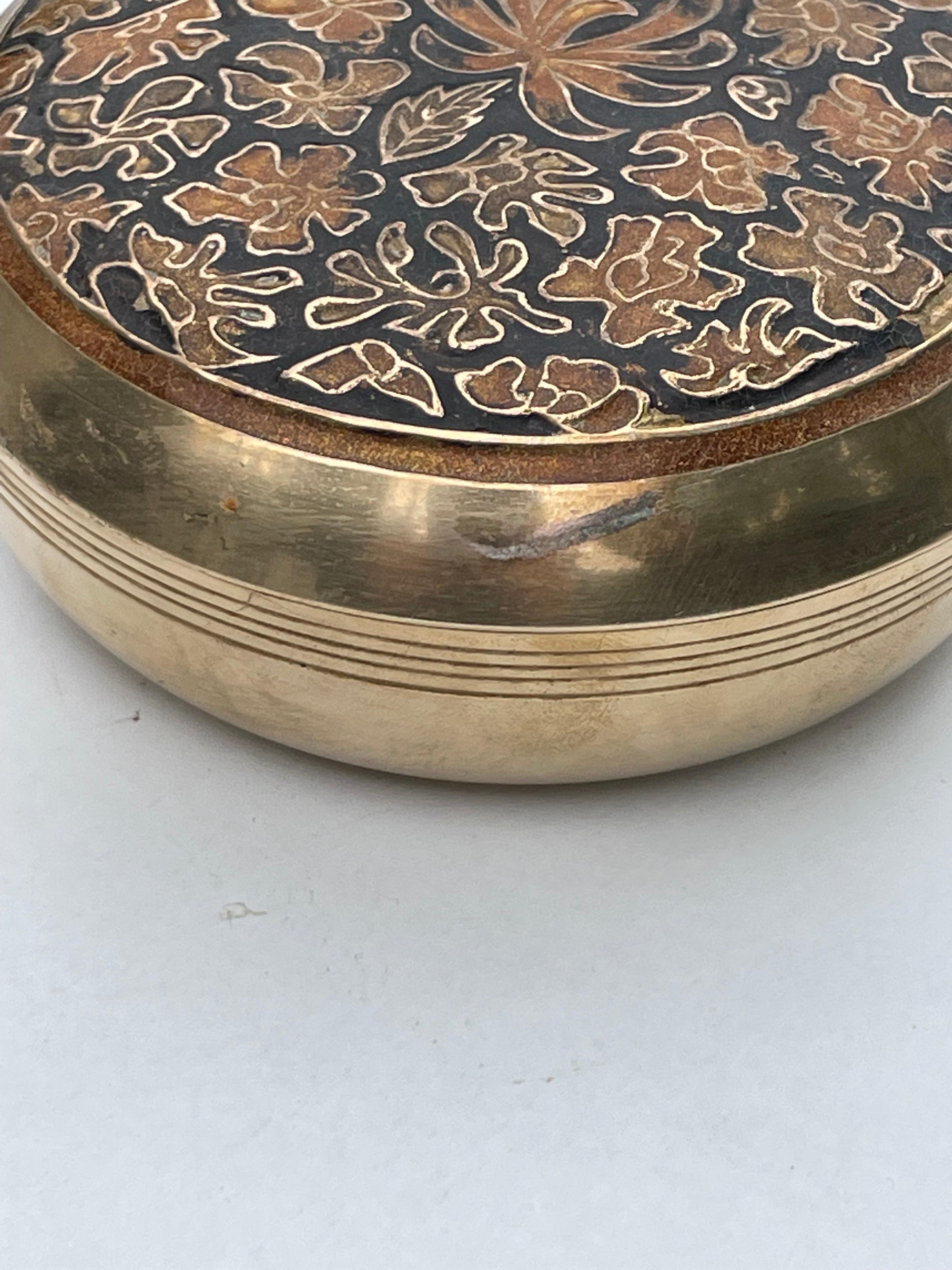This jewelry box is in brass. It has been made in france circa 1970. It has a rond shape, with colored flowers pattern. The color is gold , and the patern color is black and gold.