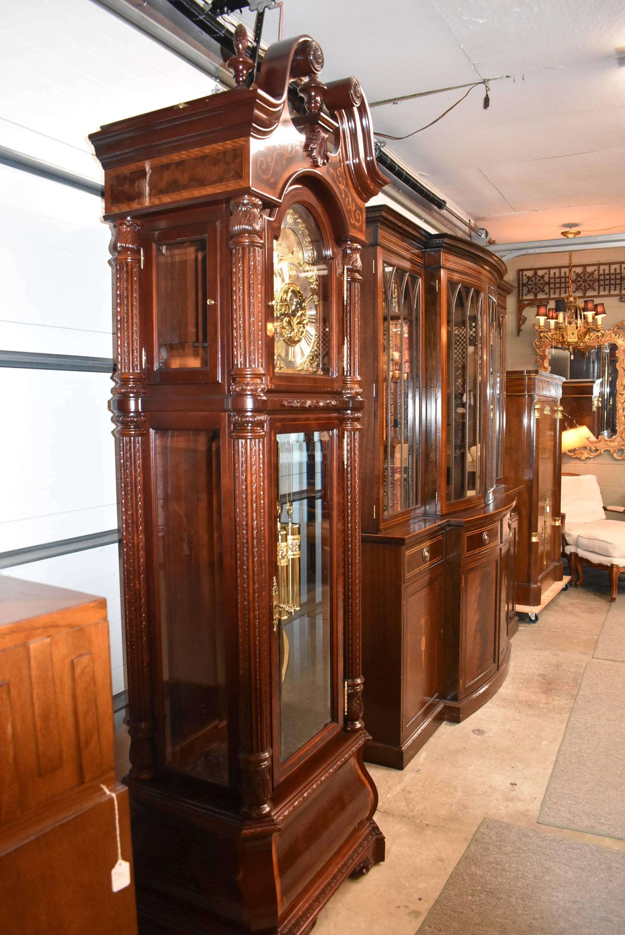 A stunning grandfather clock by Howard Miller, The J.H. Miller, 0611-030. This clock is 8 years old. This beautiful piece was finished in Windsor Cherry. The swan neck pediment is crowned with three carved finials, two carved rosettes and a carved