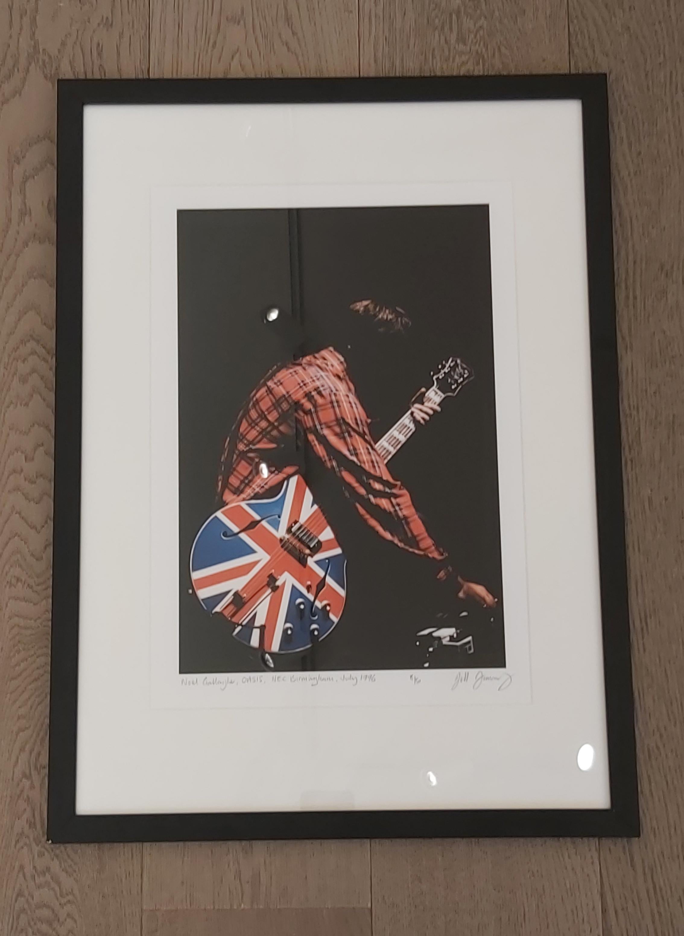 Oasis, 1996 by Jill Furmanovsky. Signed Limited Edition 15/50. 
FRAMED

Noel Gallagher of Oasis, with his signature Union Jack guitar, Birmingham, 1996.

Size A3 Archival Pigment Print, 42 x 56 x 1.5 cm framed. The image area is 23 x 35 cm, not