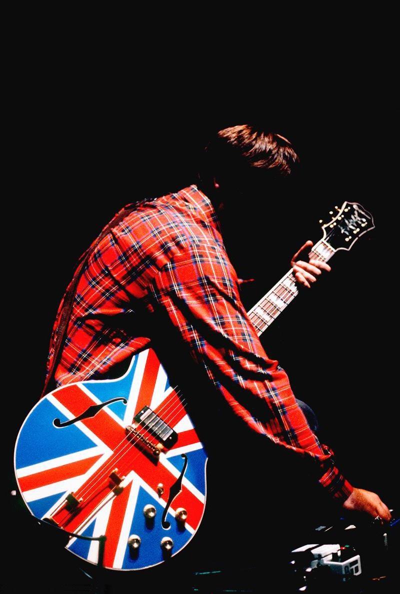 Noel Gallagher von der legendären Band Oasis, aufgenommen im NEC Birmingham, England, Mitte der 90er Jahre, aufgenommen von Jill Furmanovsky (mit seiner charakteristischen Union Jack-Gitarre). 

Signiert und nummeriert von Jill Furmanovsky in