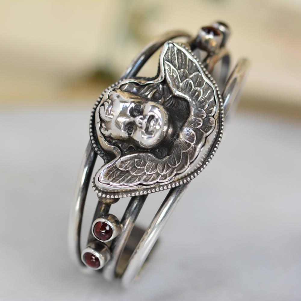 This Sterling Silver cuff bracelet features an original antique nineteenth century French figural angel with wings extended. Ornately hand framed in delicate silver beading and accented on either side with two 5 mm natural bohemian garnets. Heavenly