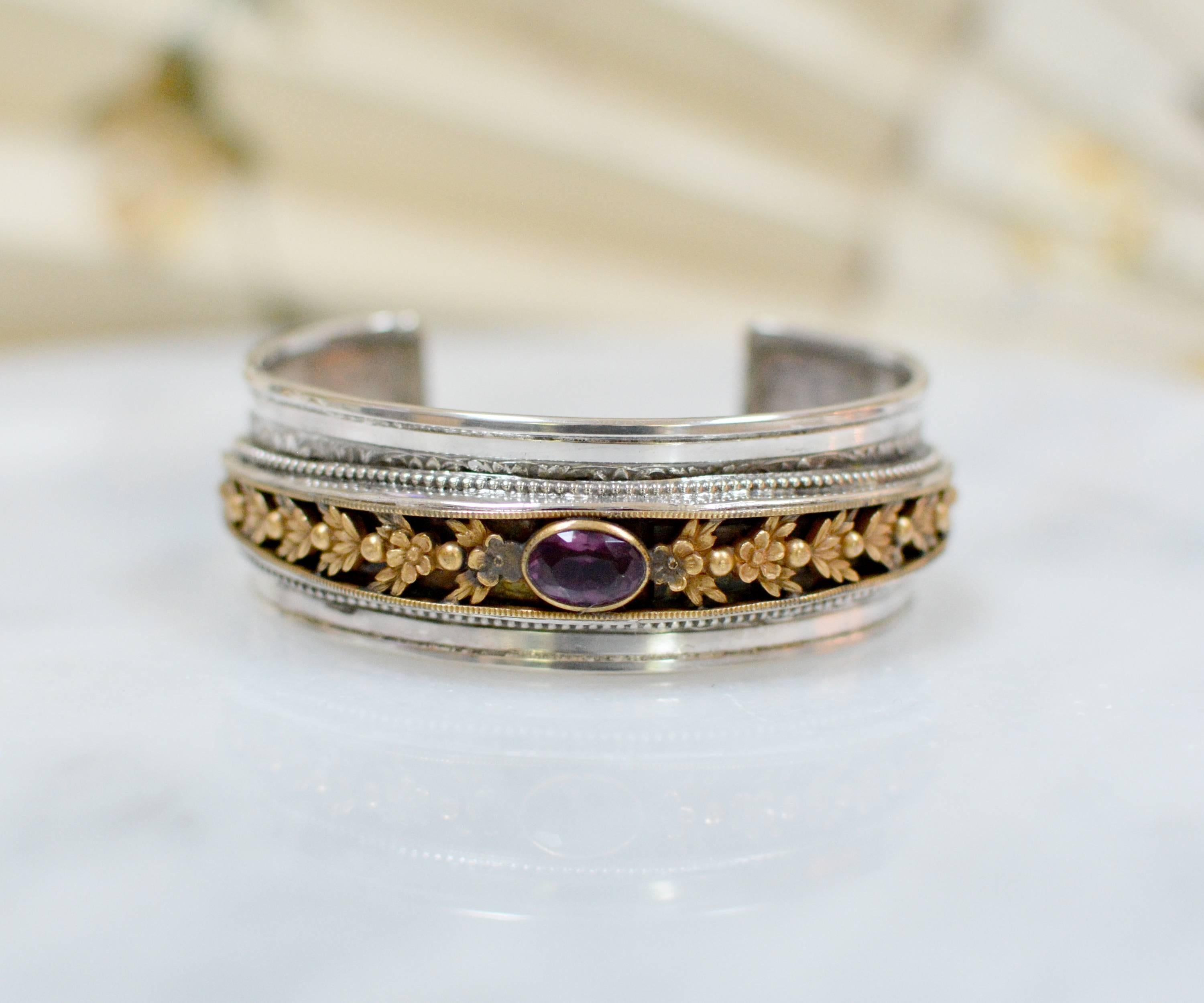 This one of a kind sterling silver cuff bracelet features a wonderful gold vermeil Art Nouveau medallion with a faceted paste amethyst. Ornate figural details of flowers and leaves gracefully trail across the length of the top. Beautifully framed