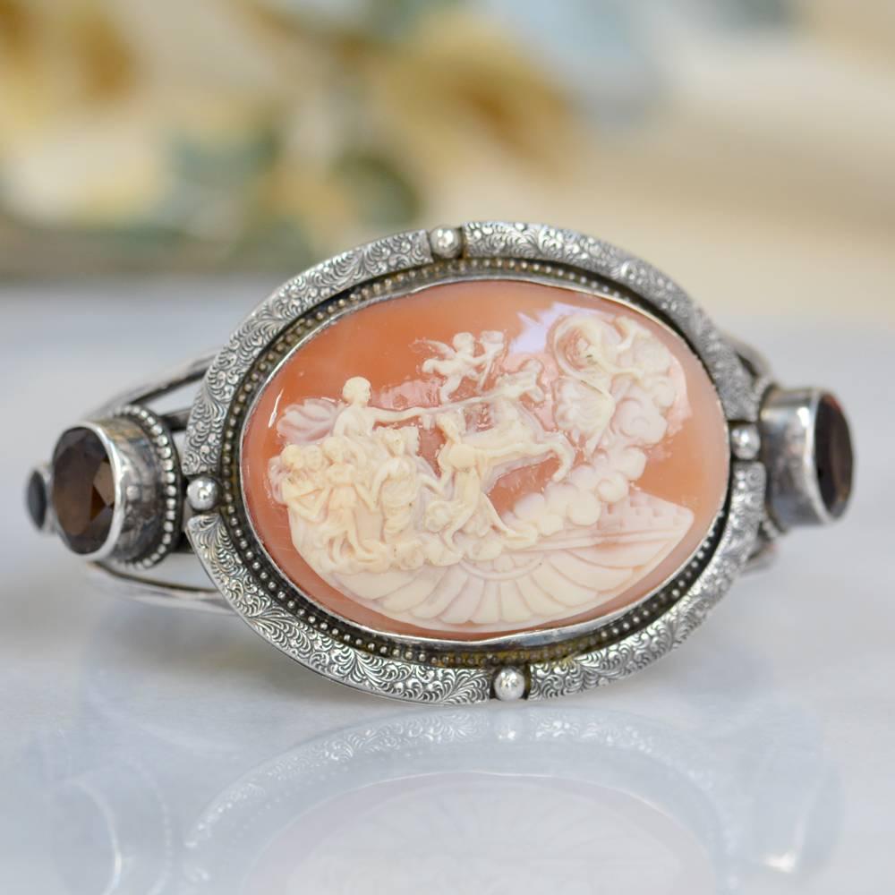 This one of a kind Sterling Silver cuff bracelet features a late nineteenth century antique hand carved shell cameo depicting a scene of angels and goddesses. Accenting this wonderful antiquity are two faceted 12 x 10 mm and two 6 mm natural faceted