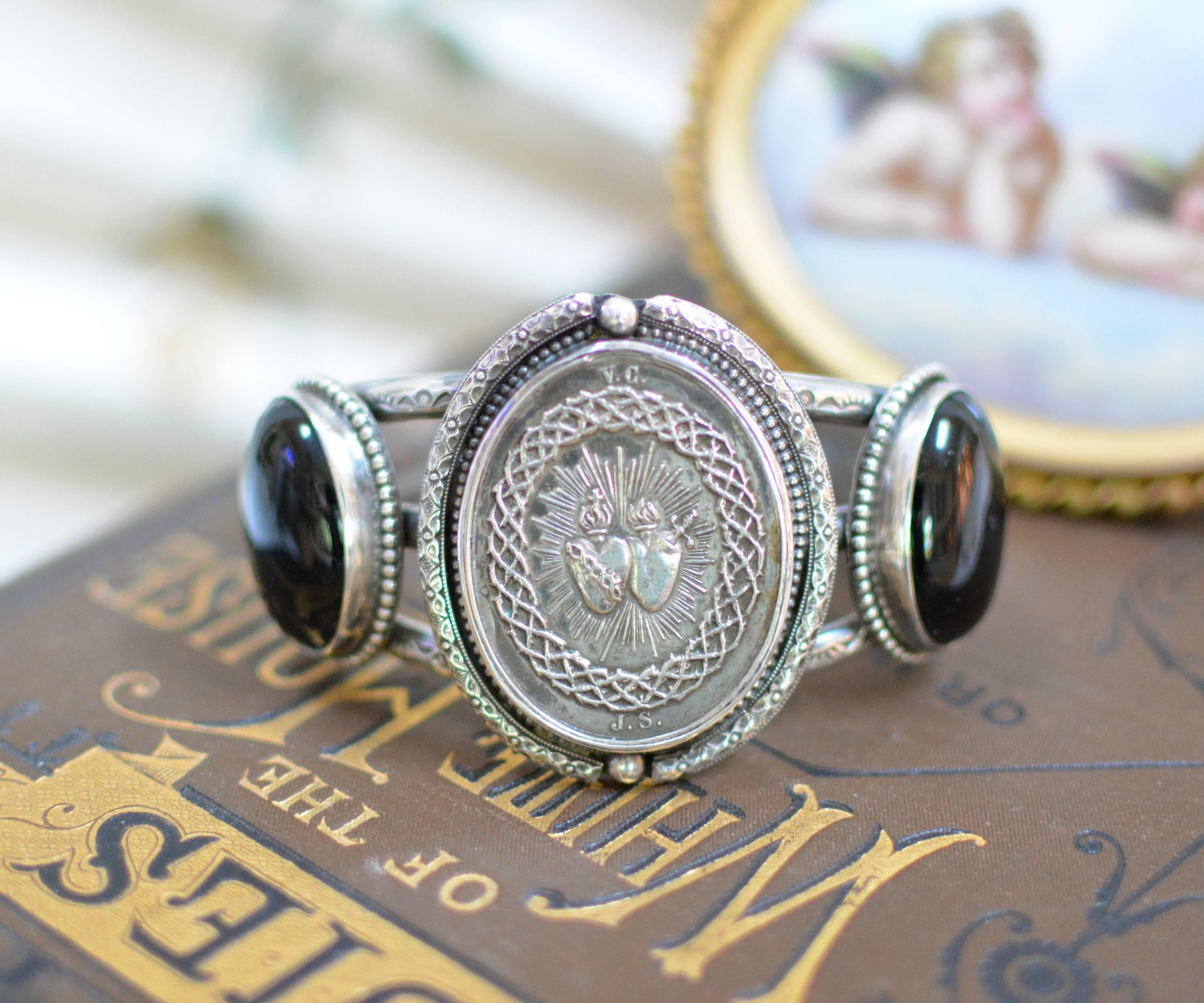 This one of a kind Sterling Silver cuff bracelet features an original antique nineteenth century French Sacred Heart Medal. Framed with ornate engraving and beadwork, we have used a pair 25 x 18 mm natural Black Onyx cabochons on either side.