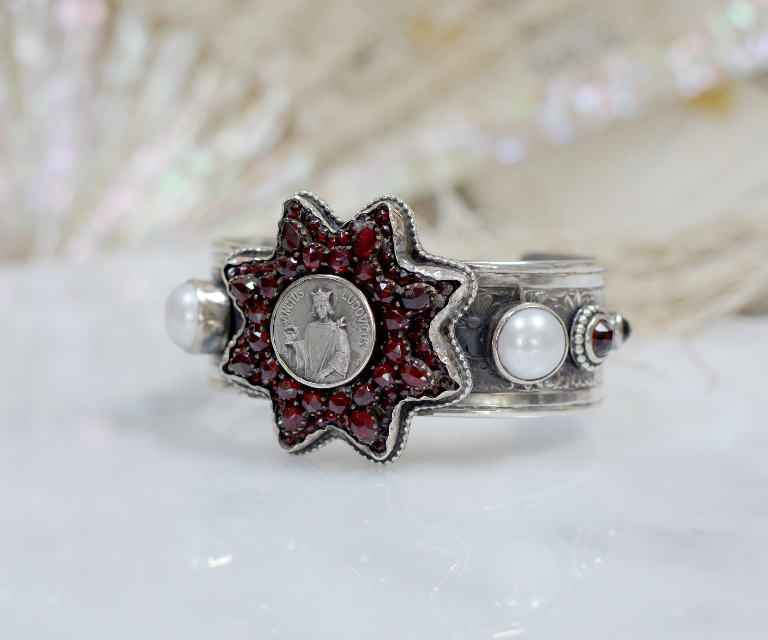 Ce trésor de bracelet de la créatrice Jill Garber présente une exquise étoile victorienne ancienne comportant environ 88 grenats de Bohême taillés en rose et sertis à la pointe. L'étoile à huit branches entoure magnifiquement une médaille religieuse