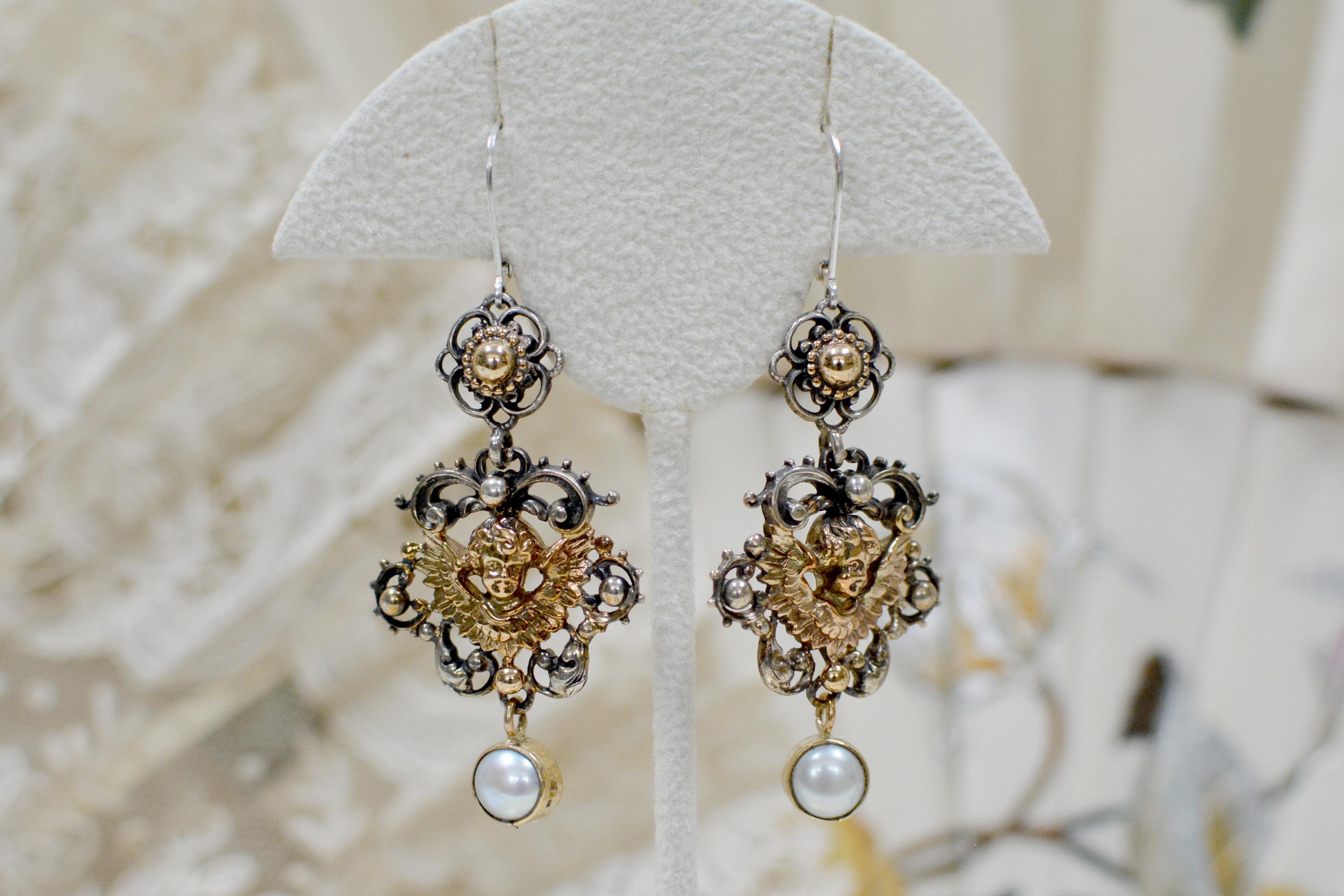 These exquisite drop earrings from Jill Garber feature complex, Baroque-style figural Angel's with outstretched wings in 14 karat gold, within an ornate sterling silver ribbon wreath. Each earring has a large, Freshwater pearl 14, karat gold drop.