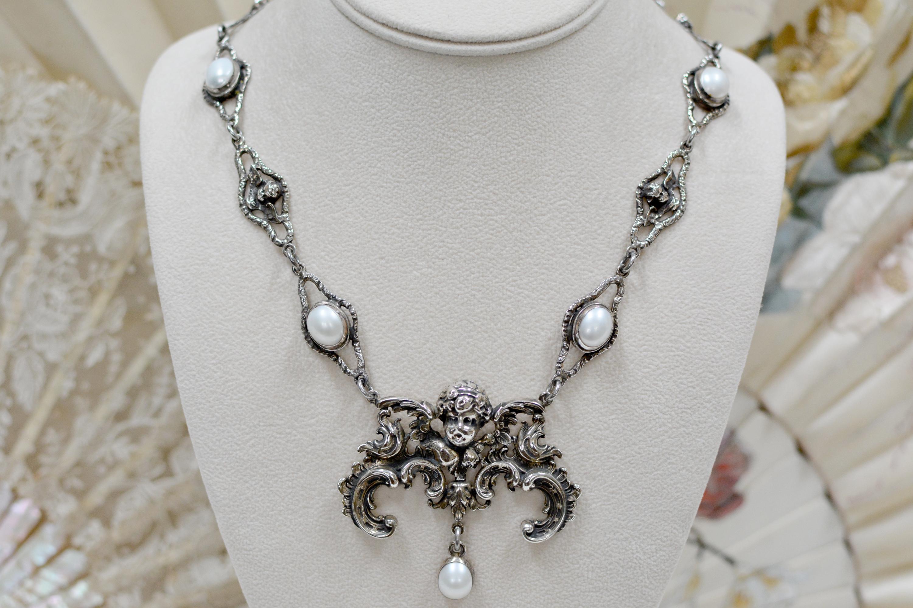 This one of a kind sterling silver drop necklace accentuates heavenly elements found in adornments throughout history. A grand figural angel establishes a bold center element for the necklace, which has a single 12 x 10 mm oval Freshwater pearl