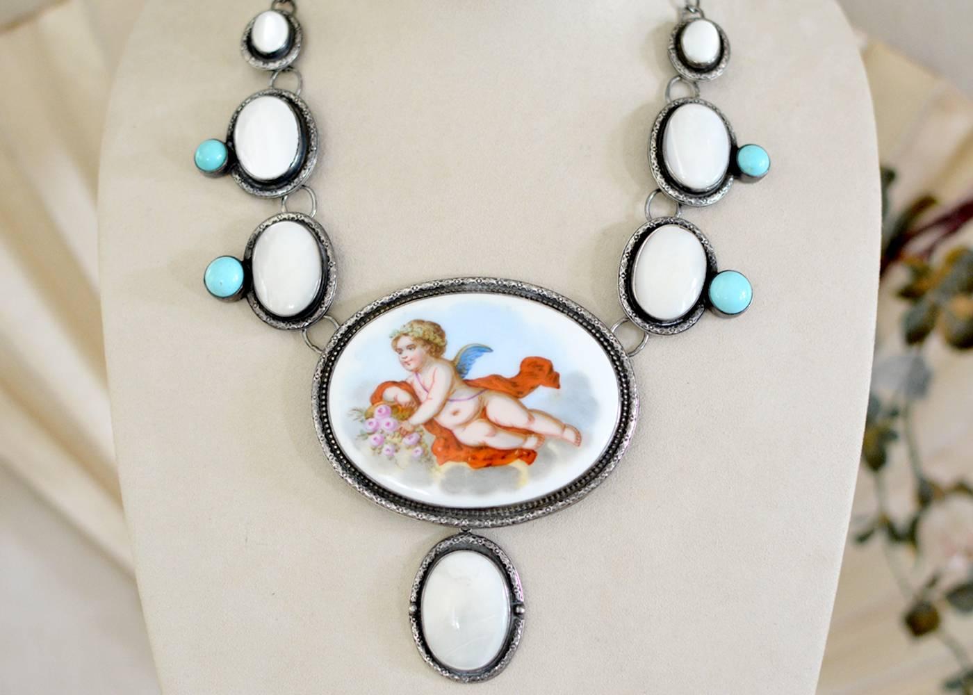 A romantic large antique French hand painted porcelain depicting a cherub cradling a basket of pink roses dating to the nineteenth century stands front and center in this one of a kind necklace. The grande 30 x 22 mm high dome natural