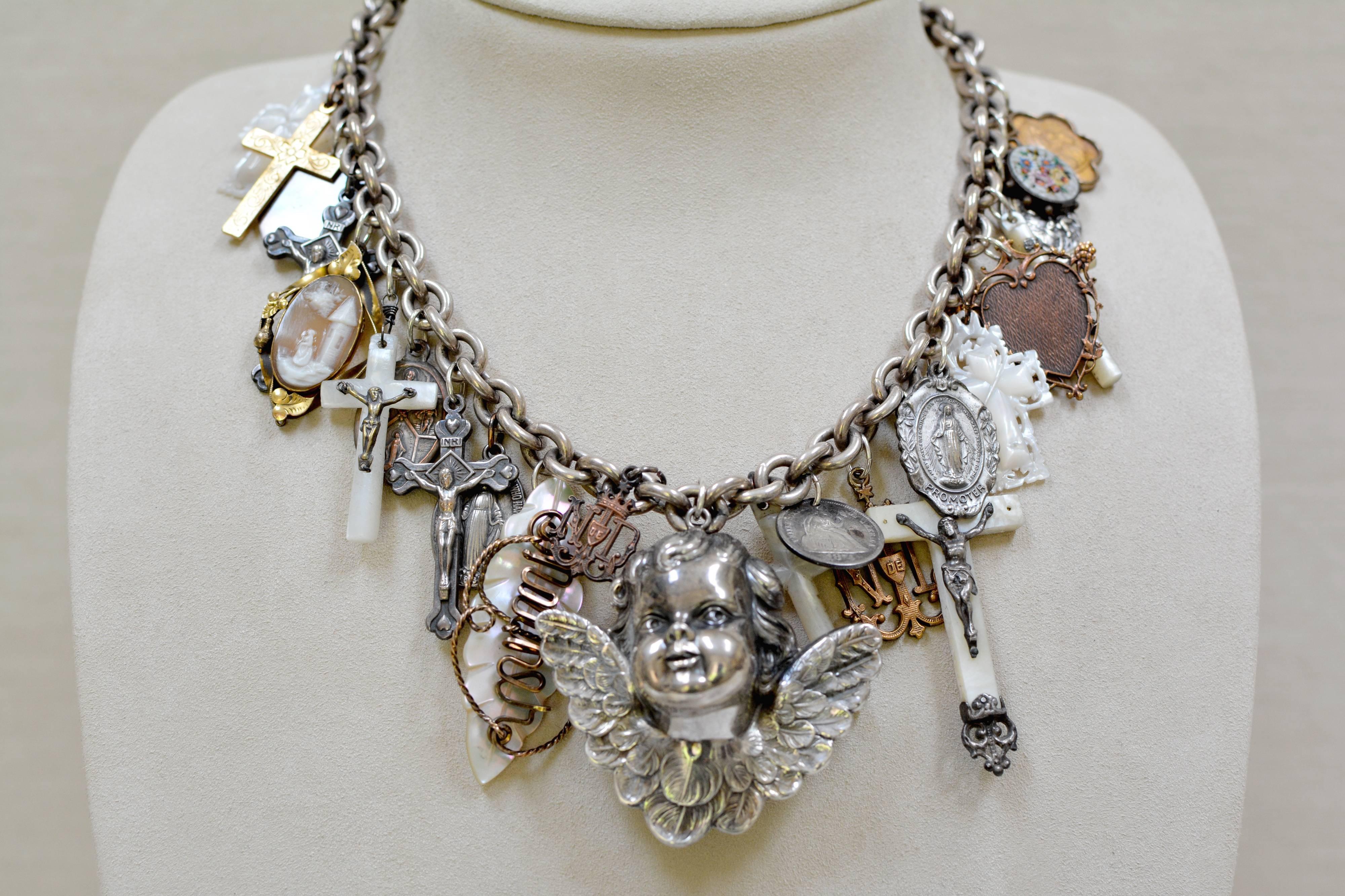 At the center of this one of a kind Love Token Festoon necklace is a large sterling silver antique figural winged cherub angel. With incredible charms and sacred treasures throughout a bold sterling silver chain. Carved Mother-of-Pearl Christening