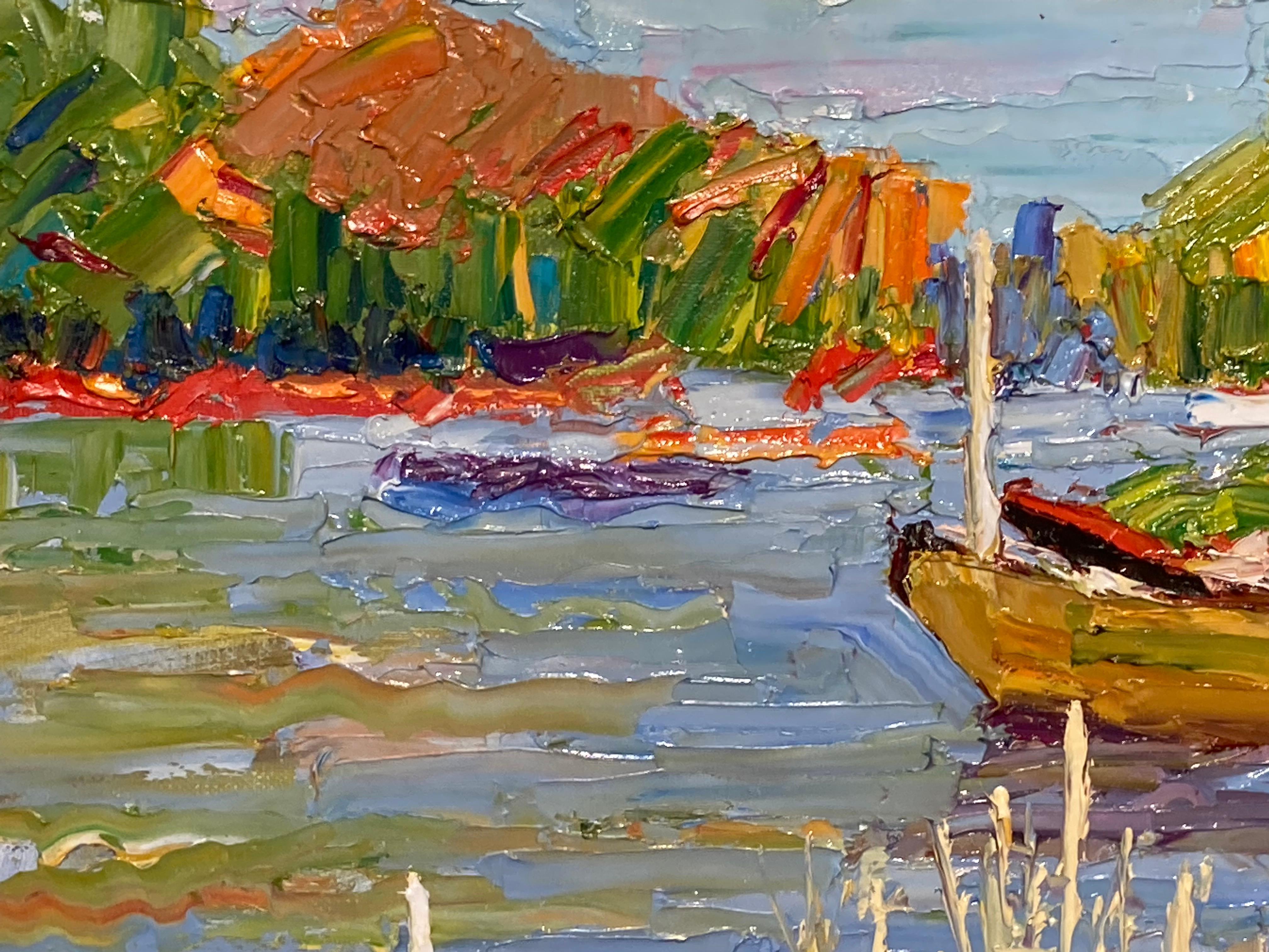 This oil on linen painting by James Cobb features several colorful row boats rested at the edge of a grassy cove. The water glistens with the light and colors on this picture perfect afternoon. The tall sandy colored grass and the subtle movements
