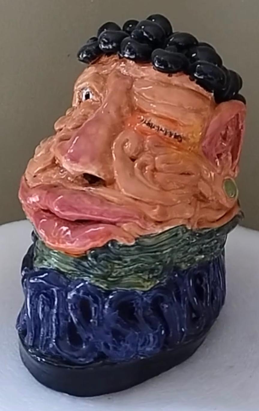 Artist: Jim Pallas (1941)
Title: Winking Mayan
Year: 2023
Medium: Pigmented epoxy and glaze on ceramic
Size: 9 x 6 x 7 inches
Condition: Excellent
Inscription: Signed and dated

JIM PALLAS (1941-) American painter, draughtsman, sculptor, and