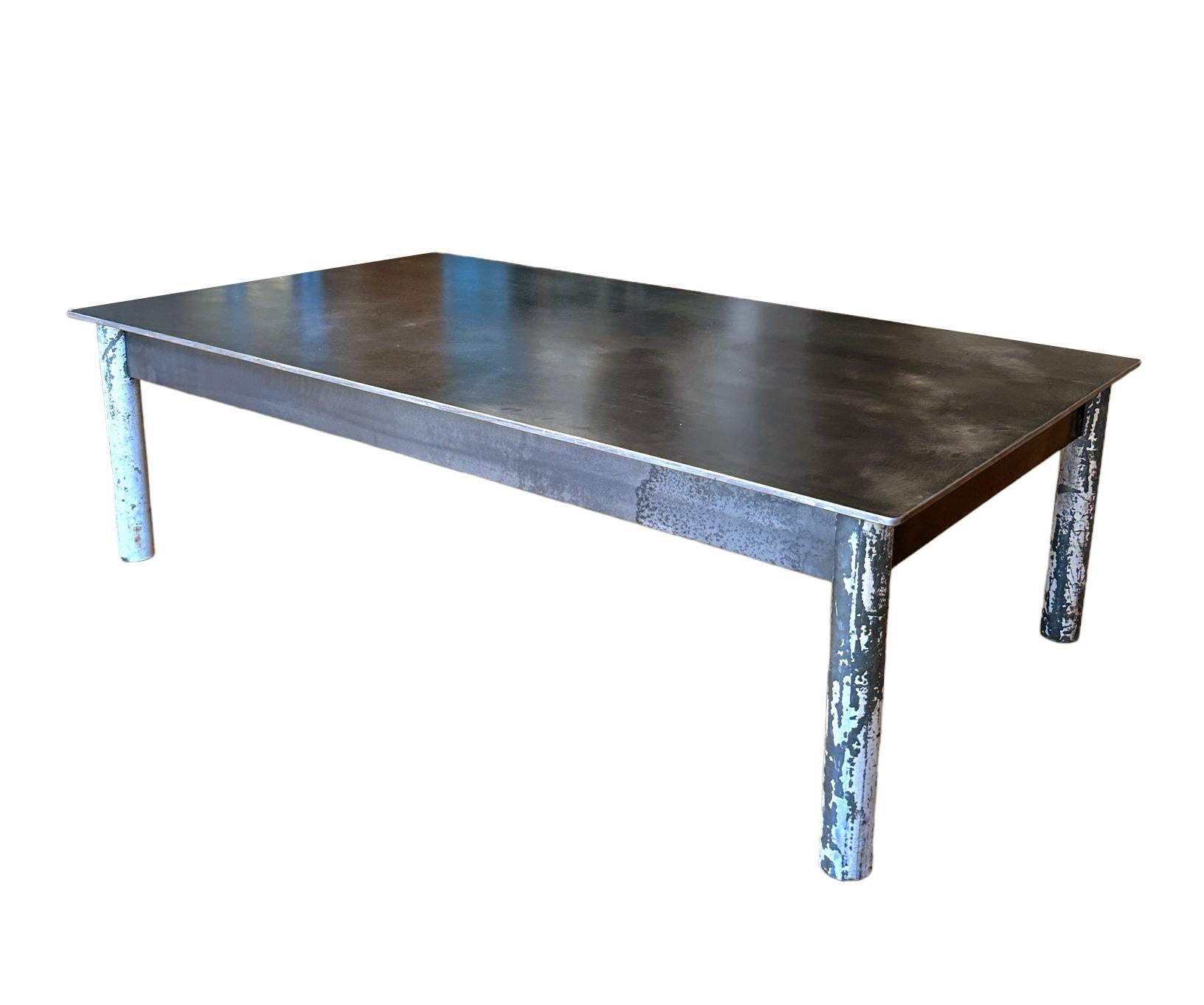 Cette table basse est fabriquée avec de l'acier laminé à chaud et des pieds en tubes d'acier réutilisés.  Les pieds étaient auparavant peints, mais l'artiste les a sablés et a conservé une grande partie de la peinture pour ajouter à l'esthétique