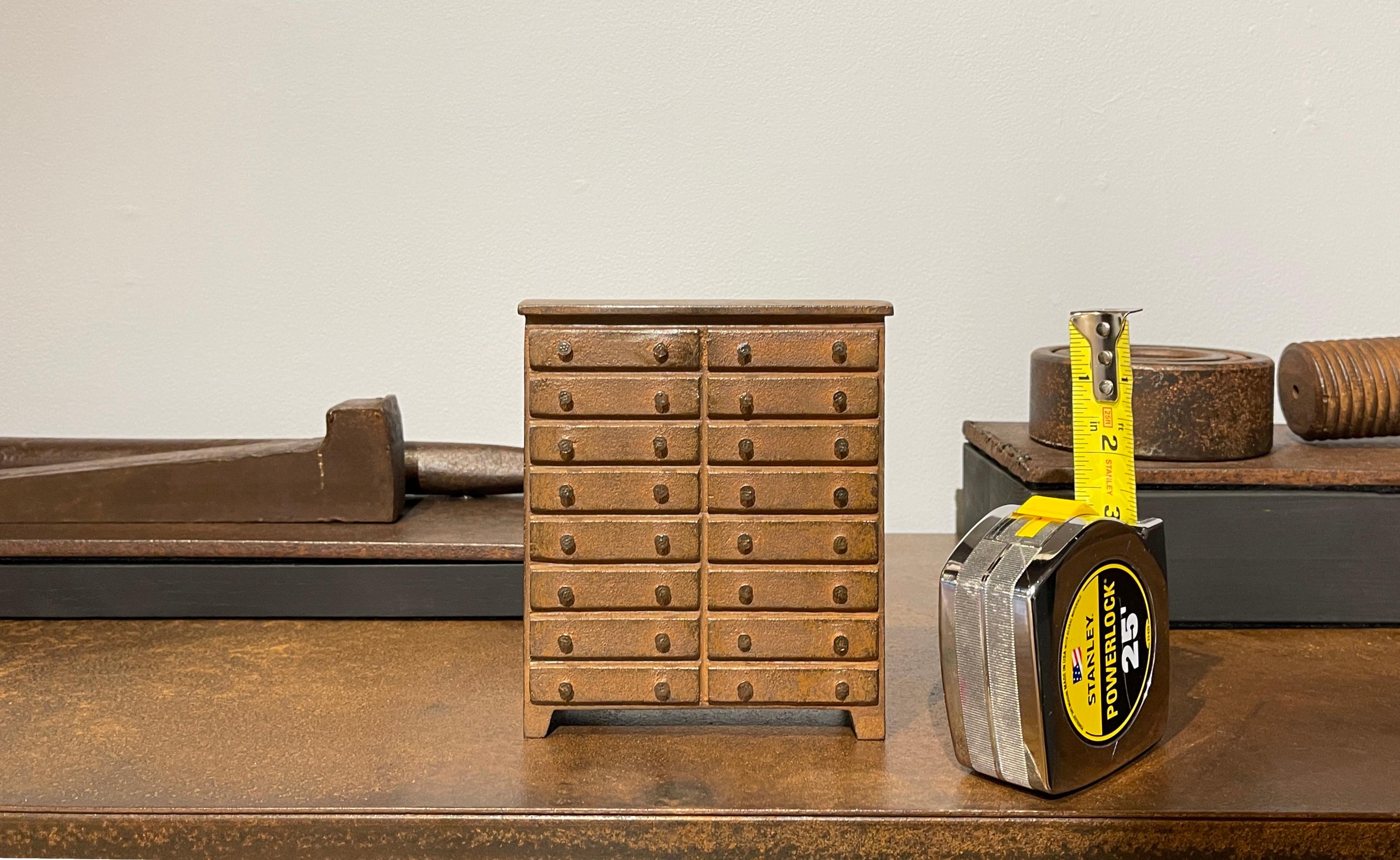 This exquisite miniature chest of drawers is inspired by Shaker furniture. Made from solid cast iron with a natural rust patina and vintage nail heads for the drawer pulls, The artist created this sculpture during an artist residency at the John