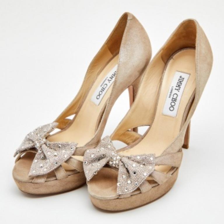Presented by the House of Jimmy Choo, these pumps define poise and grace with their elegant exterior. They are crafted from beige suede and flaunt a crystal-embellished bow accent on the front, peep-toes, cut-out details, and platforms. They are