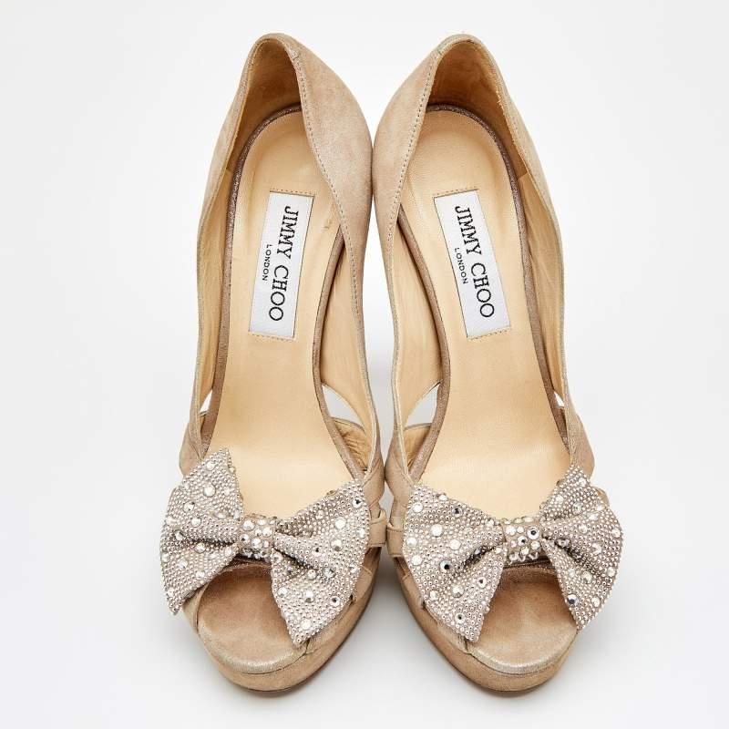 Presented by the House of Jimmy Choo, these pumps define poise and grace with their elegant exterior. They are crafted from beige suede and flaunt a crystal-embellished bow accent on the front, peep-toes, cut-out details, and platforms. They are