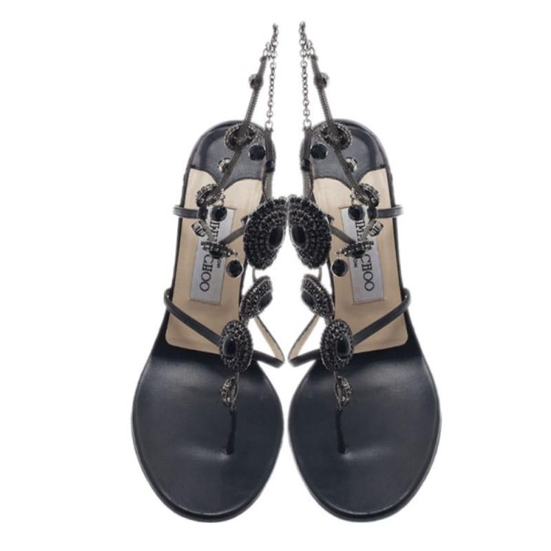 These Jimmy Choo sandals look like a beautifully hanging chandelier. Their dainty design features black leather straps, thong toes, and vamps embellished with jeweled brooches on dark silver-tone chains and a back ankle strap. Their beige