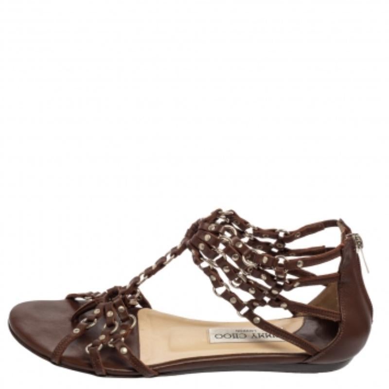 Experience comfort and luxe style both as you wear these caged flat sandals from the House of Jimmy Choo. They are made from brown leather, which is enhanced with studded accents. They flaunt a T-strap detail, silver-toned hardware, and zipper