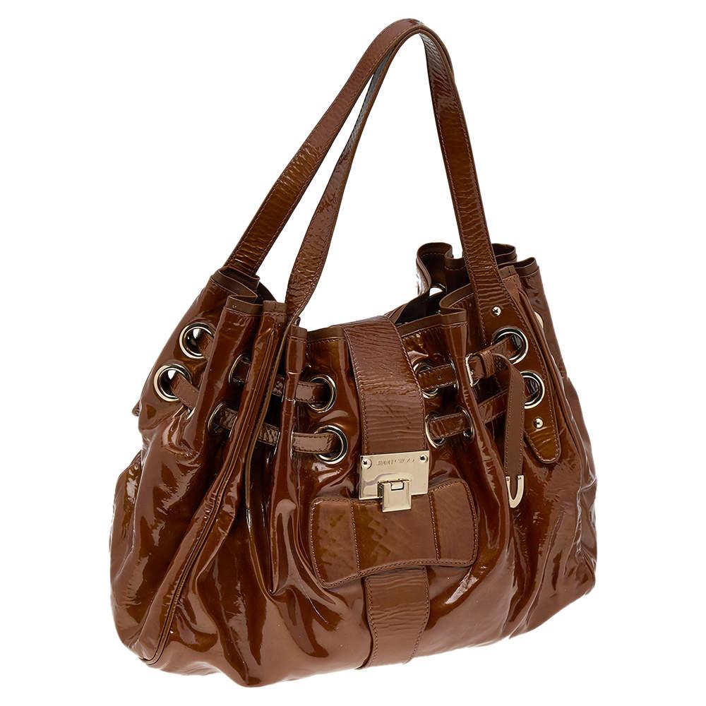 Own this gorgeous Jimmy Choo Riki bag today and light up your closet! Crafted from patent leather, this stunning brown number has a flap top with a signature lock and a spacious Alcantara interior. It also features two top handles, gold-tone