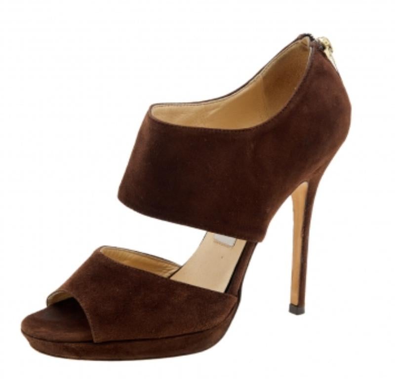 Derrocha clase y perfección al caminar con estas sandalias de Jimmy Choo. Están confeccionadas con ante marrón en el exterior. Presentan puntera abierta, herrajes dorados y tacón superfino. Tienen cierre de cremallera. ¡Luce un estilo impresionante