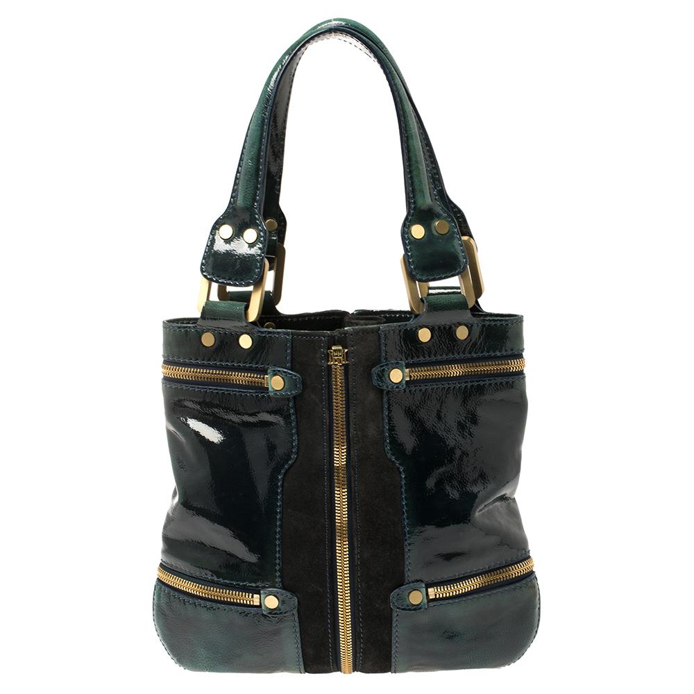 This keep-it-all bag from the fashion label Jimmy Choo is uniquely designed. Crafted from patent leather and suede, this dark green bag features zip pocket designs and rolled handles. The spacious bag opens to a suede-lined interior that has enough