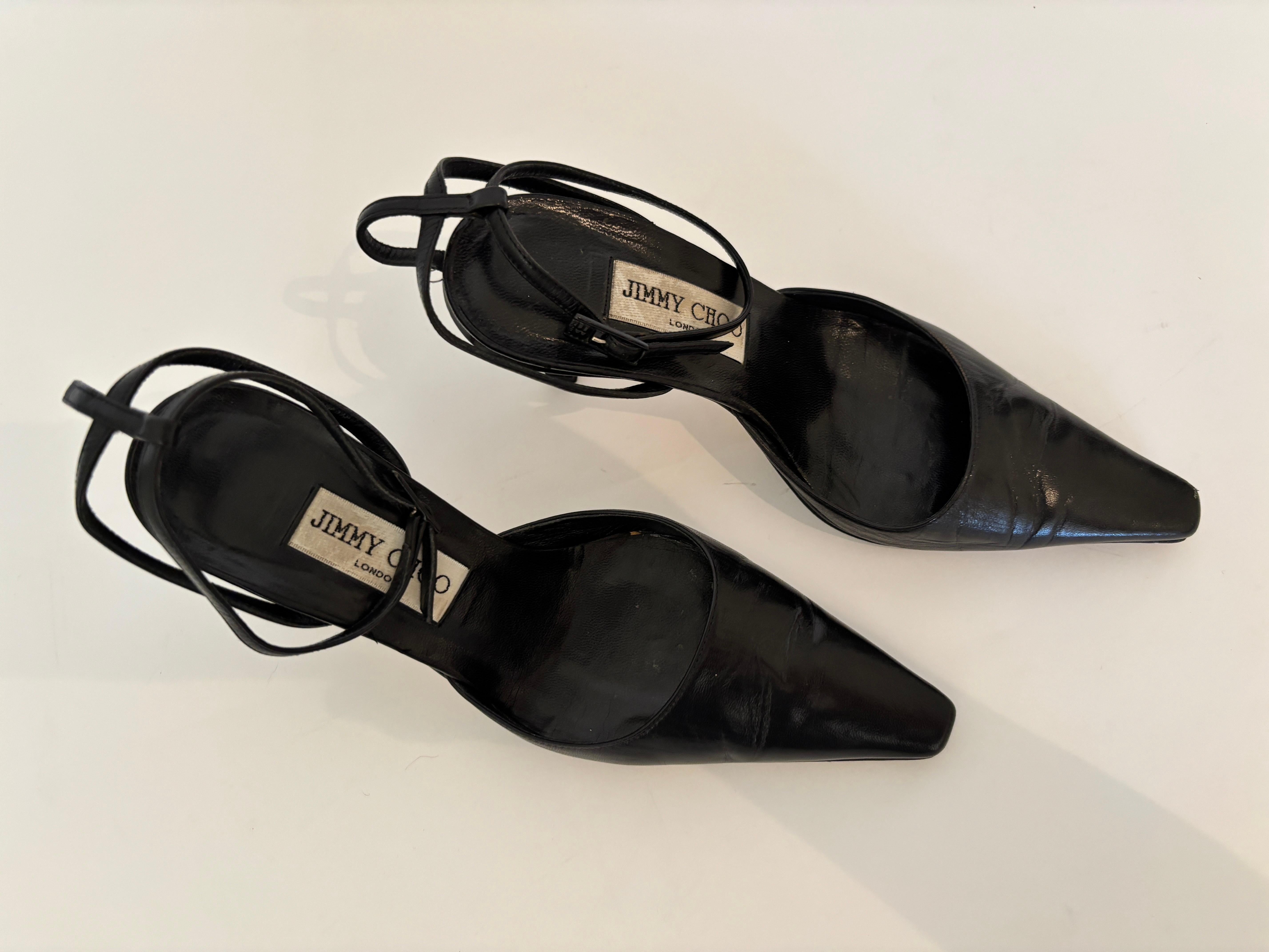 Eleva la tua collezione con questi tacchi slingback in pelle nera vintage di Jimmy Choo, realizzati in Italia e caratterizzati da un caratteristico cinturino circolare alla caviglia con fibbia regolabile. Queste classiche décolleté con punta