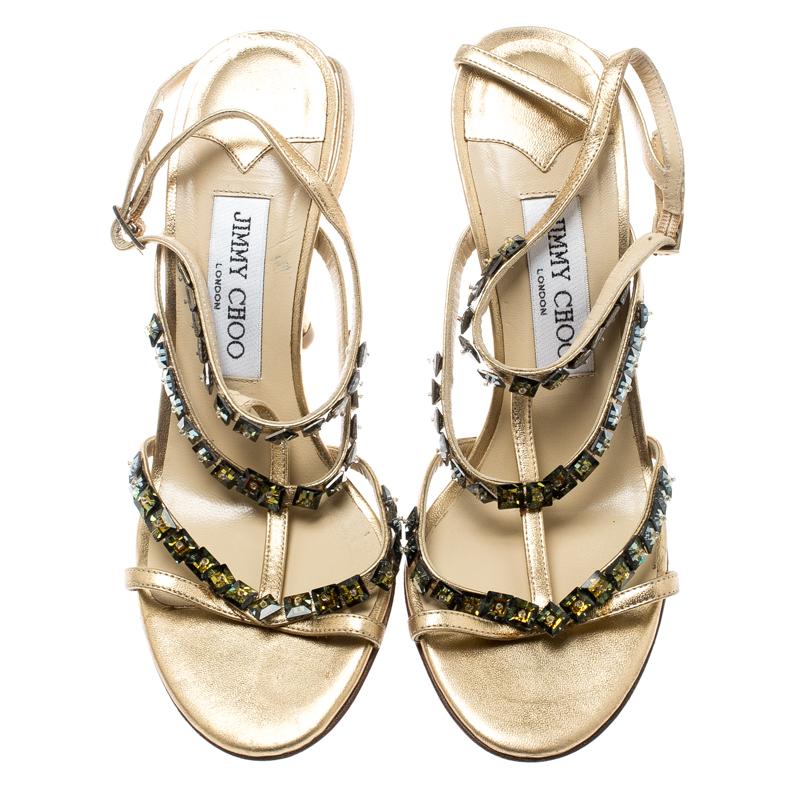 Styled with stunning crystal embellishments, this metallic gold Jimmy Choo number is crafted in leather as a T-strap and completed with buckle closures at the ankles. The strappy design on the piece, coupled with 10 cm heels makes it a pair that's
