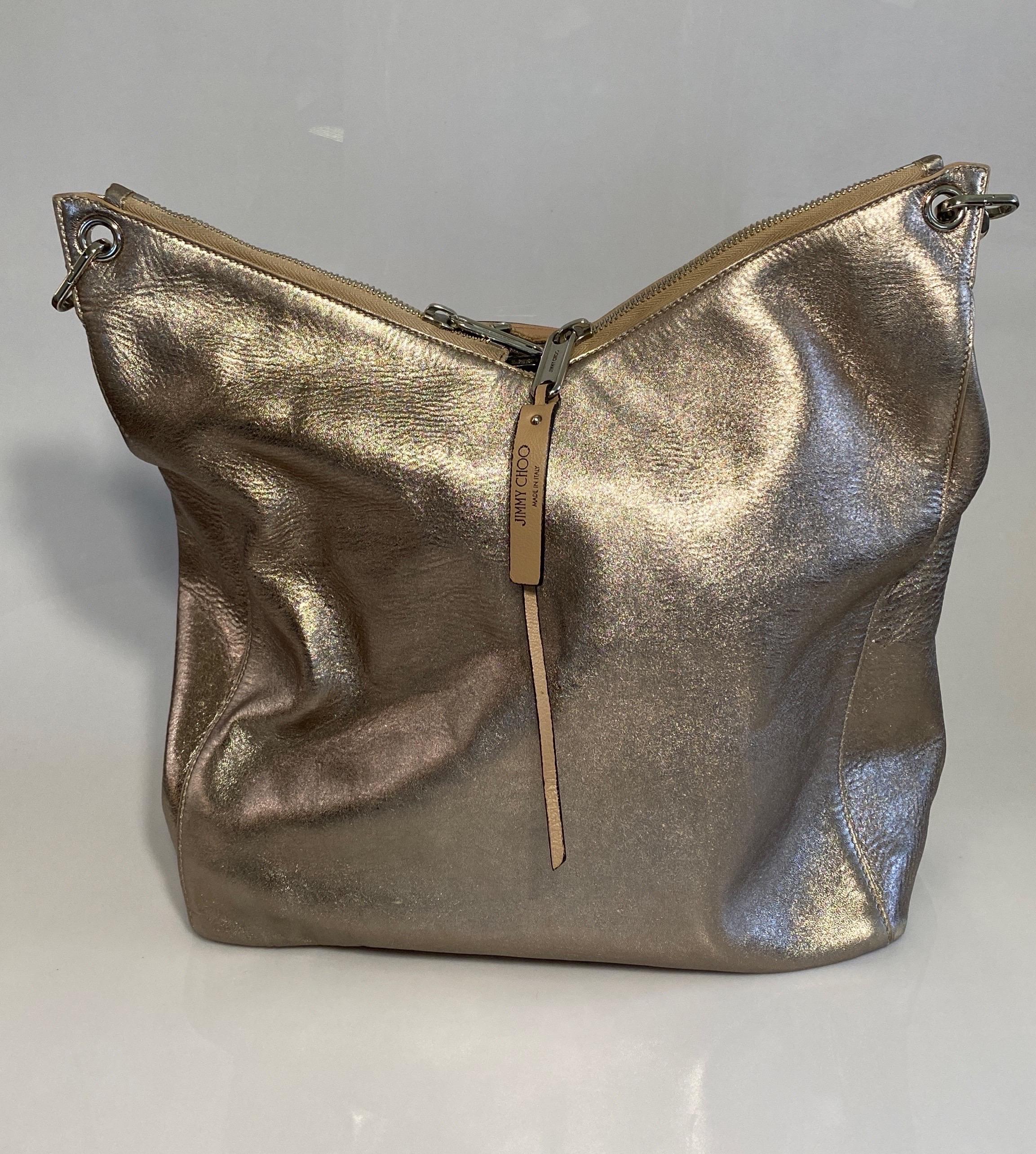 Jimmy Choo Metallic Large Hobo Tote has a bronze/gold tone to it. The leather has that distressed look to it. The top of the bag has a V Shaped dual zip closure with a hanging leather Jimmy Choo accessory detail. It has a Silver large link and