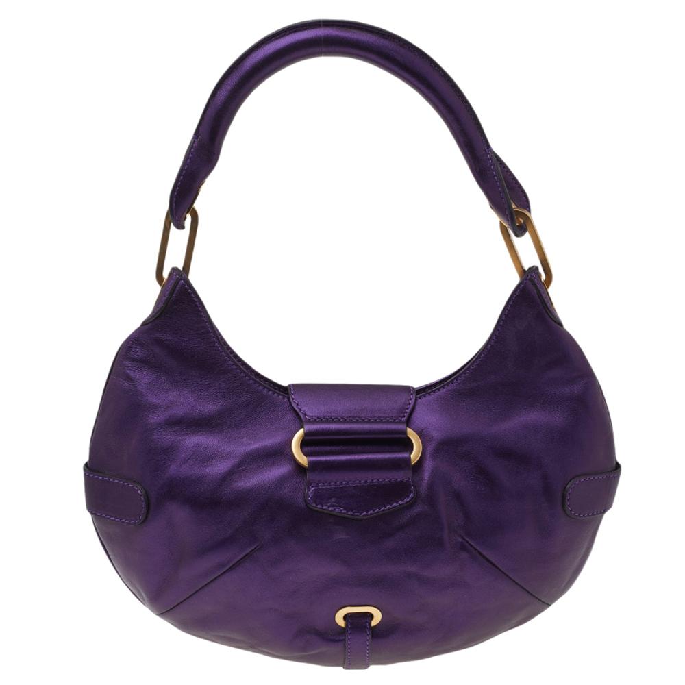 This Jimmy Choo Tulita hobo bag has a stunning exterior crafted in metallic purple leather accented with gold-tone hardware, a flap closure, two shoulder straps, and buckle detailing. Its interior is lined with Alcantara and has brand