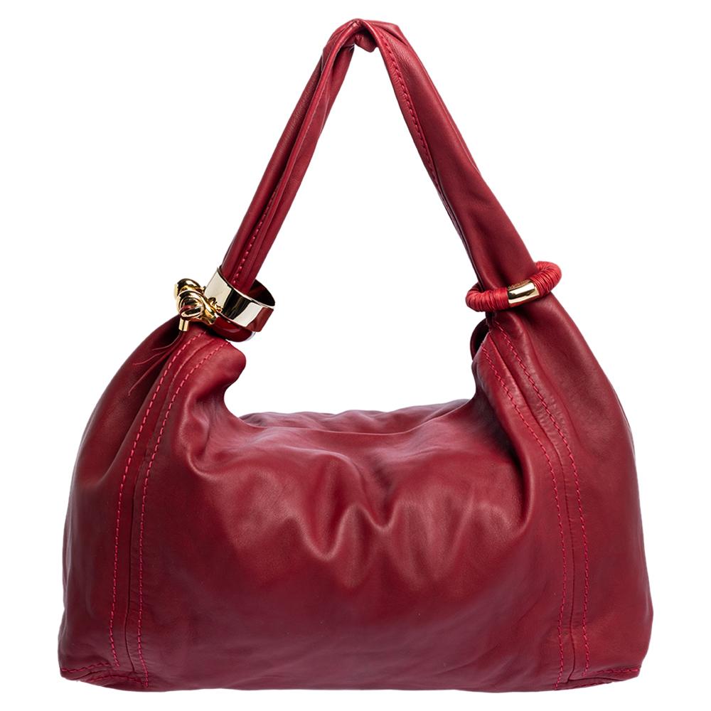 This lovely Saba hobo comes from the iconic house of Jimmy Choo. Crafted in Italy, it has been made from leather in a lovely red hue. It is held by a single handle that is beautified with a gold-tone accessory. The bag opens to a spacious