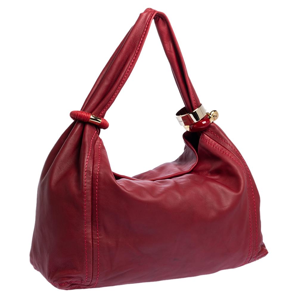 This lovely Saba hobo comes from the iconic house of Jimmy Choo. Crafted in Italy, it has been made from leather in a lovely red hue. It is held by a single handle that is beautified with a gold-tone accessory. The bag opens to a spacious