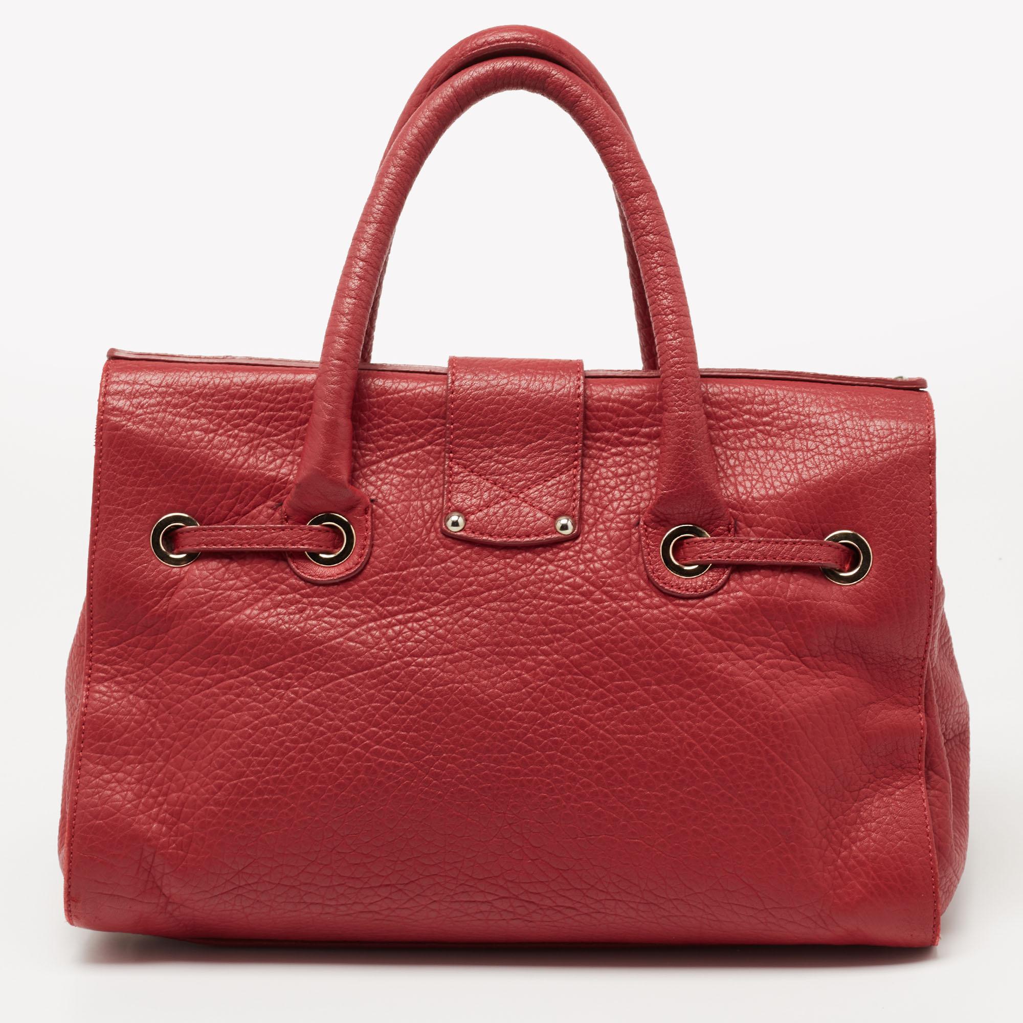 This Jimmy Choo Rosalie is a practical handbag with a luxe touch. Crafted from leather, it has a red shade, an engraved flip closure in gold-tone hardware, dual top handles, a removable shoulder strap, and protective feet at the bottom. Finished