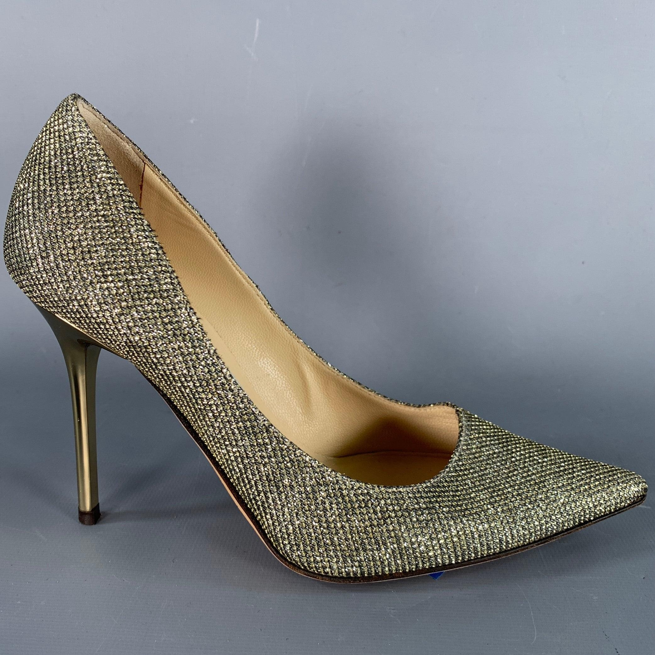 JIMMY CHOO pumps in a gold tone glittered fabric featuring a gold tone metal stiletto heel, pointed toe, and slip on closure. Made in Italy.Very Good Pre-Owned Condition. 

Marked:   IT 34 

Measurements: 
  Heel: 3.75 inches 

  
  
 
Sui Generis