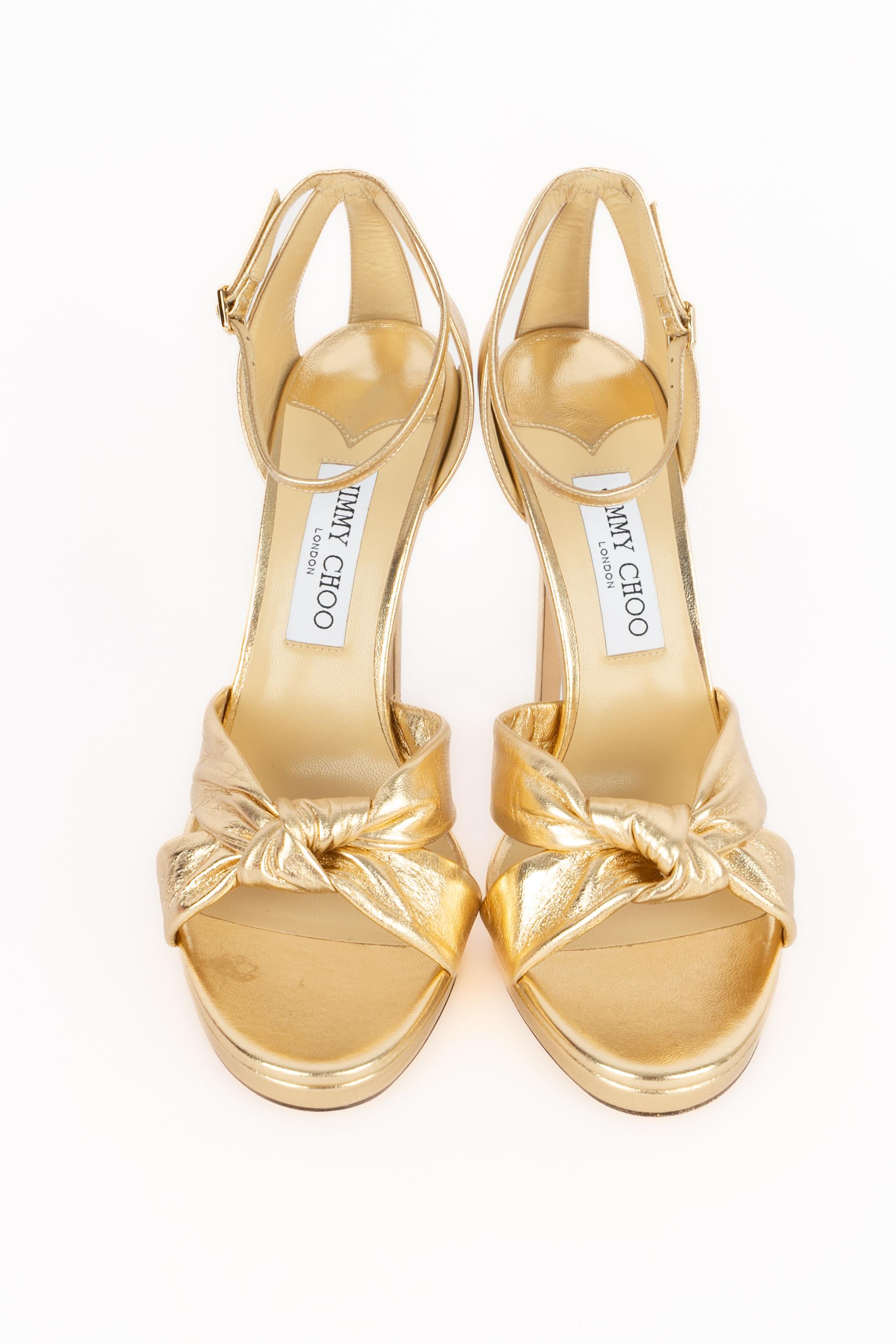 JIMMY CHOO - (Made in Italy) Zapatos de tacón de aguja de napa dorada con lazo delantero. Brida de tobillo y plataforma pequeña. Se indica la talla 40FR.

Estado:
Muy buen estado

Dimensiones:
Altura del tacón: 13 cm

SKU:CH115