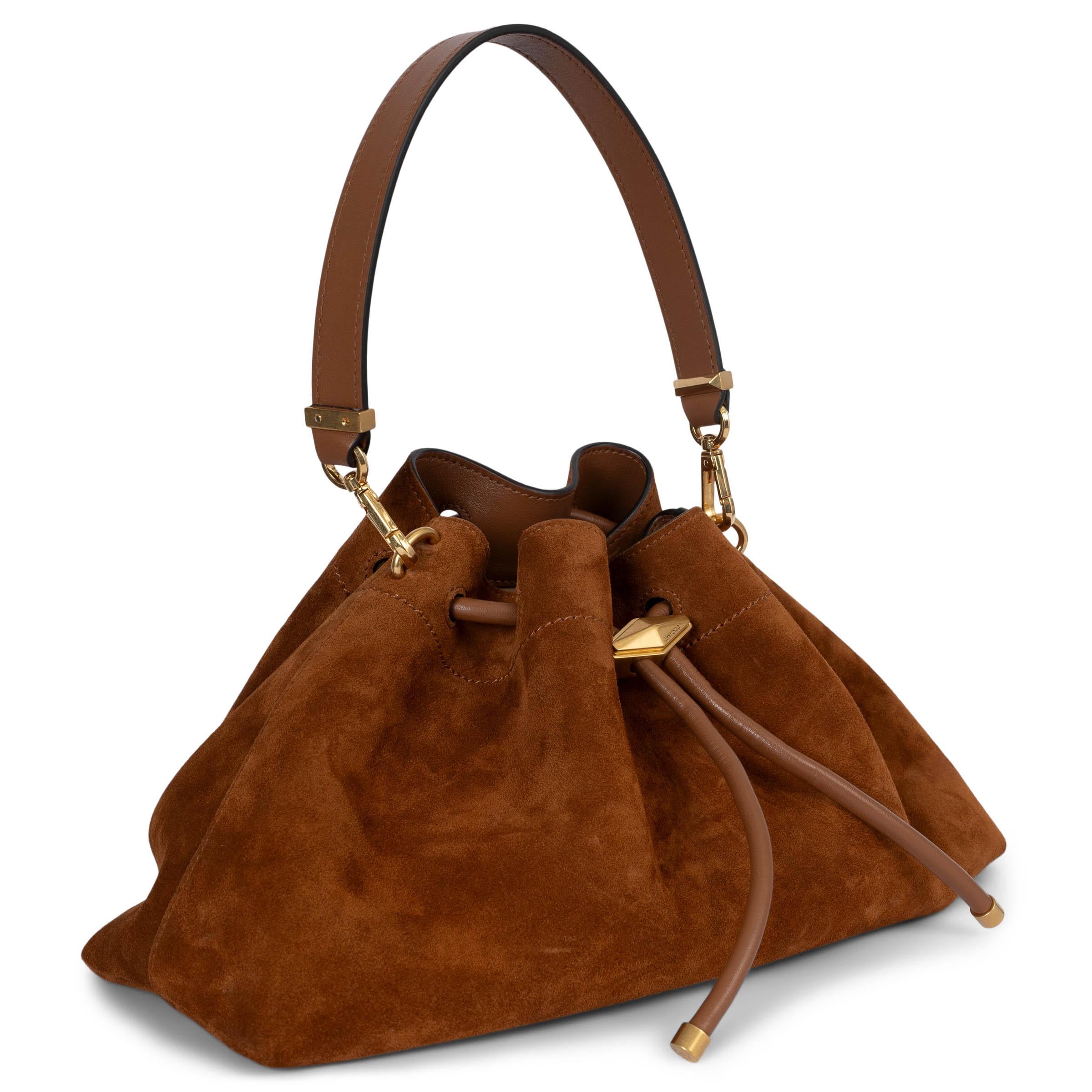 This 100% authentic Jimmy Choo Cinch M handbag is crafted from luxurious tan suede and features elegant gold-tone hardware. The unique silhouette is cinched by a stunning faceted Diamond drawstring closure, adding a touch of glamour. The interior is