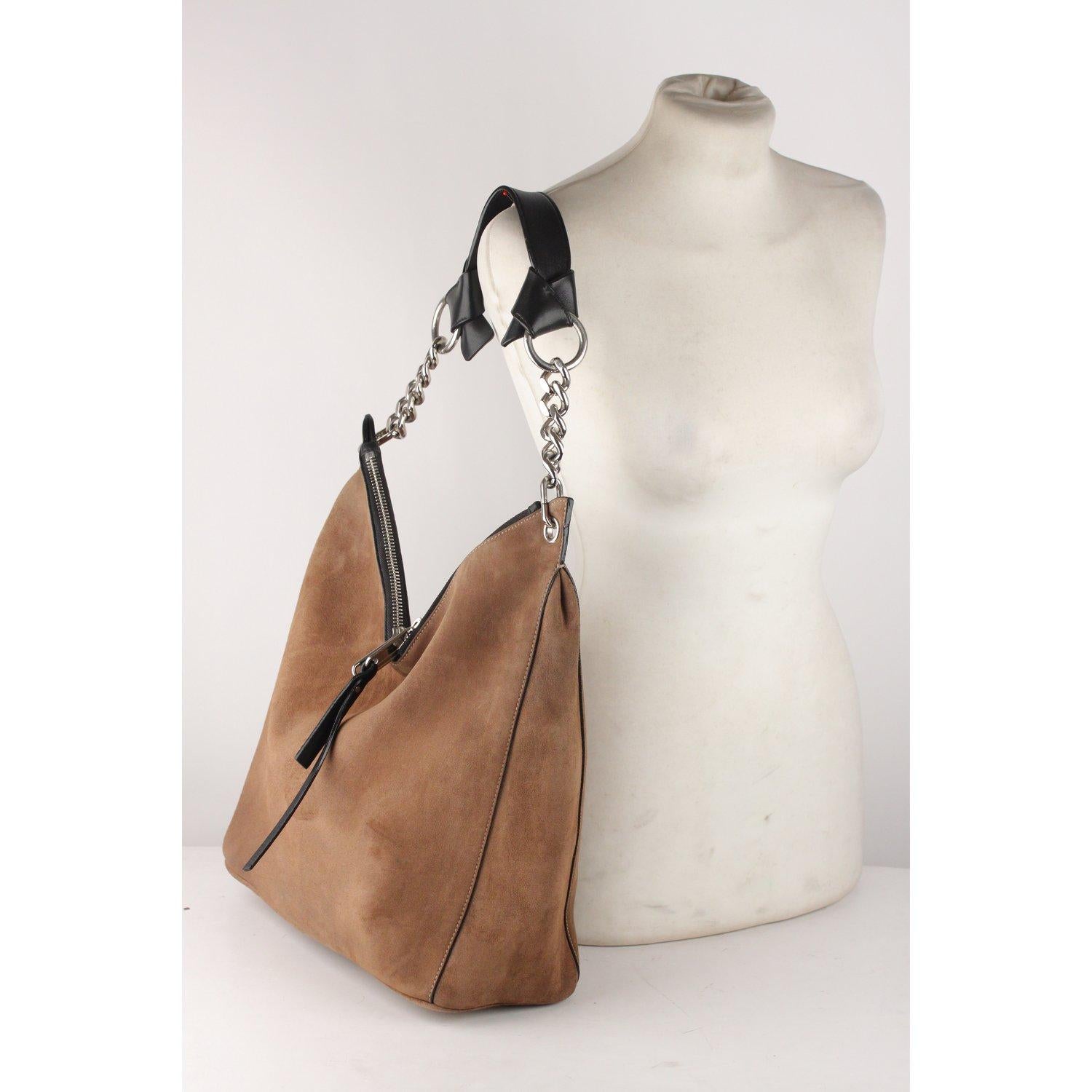 Jimmy Choo’s Raven shoulder bag crafted in tan suede with silver metal chain strap and black leather strap with knotted detail. Double zipper closure with embossed logo zipper pull. Fully lined in suede. 1 side pocket with button closure inside.