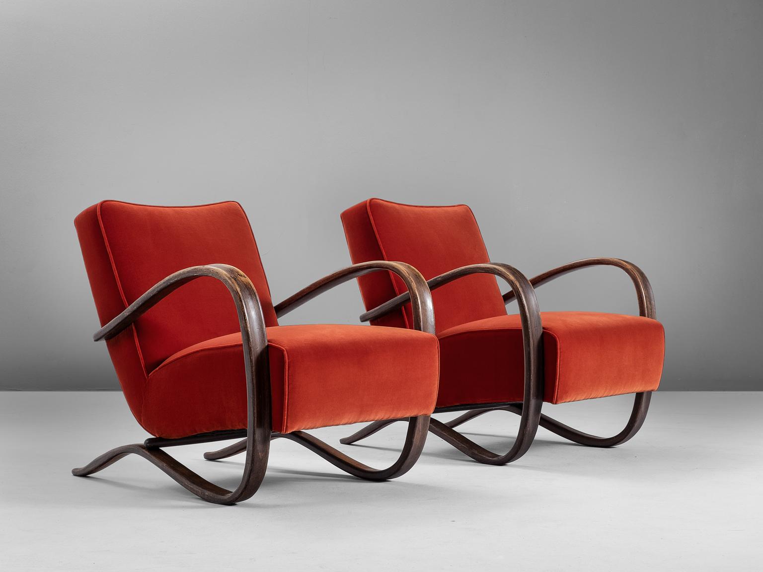 Jindrich Halabala, armchairs, beech and fabric, by Czech Republic, 1930s. 

These chairs have a very dynamic appearance, due the curved base that ends fluently in the armrests. The dark brown stained wood nicely combines to the red velvet like