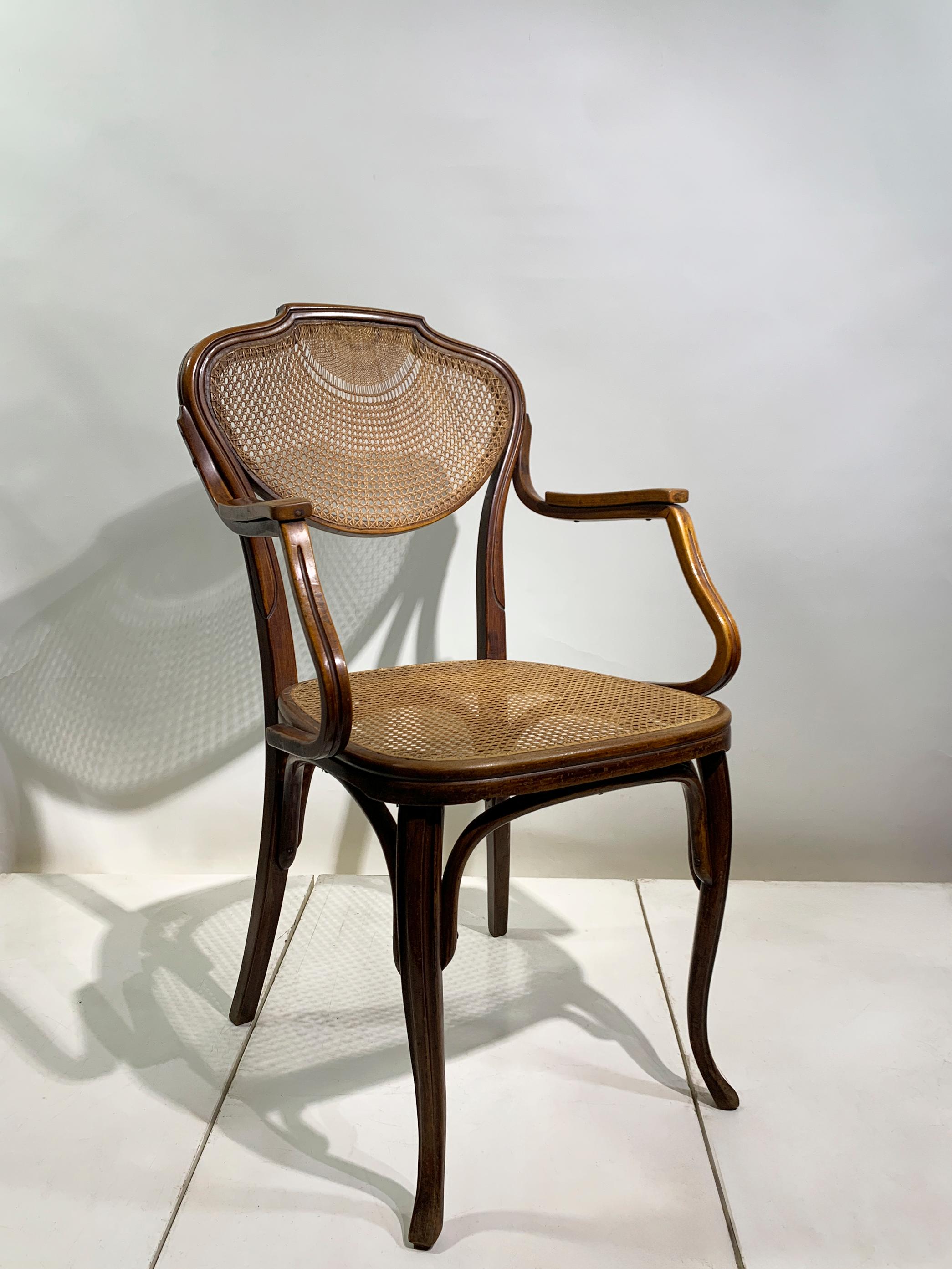 An elegant bentwood armchair by the renowned Austrian manufacturer J&J Kohn, dating to the turn of the 20th century. This chair features the iconic steam-bent beechwood frame with a rich, dark finish and a finely woven cane (rattan) seat and